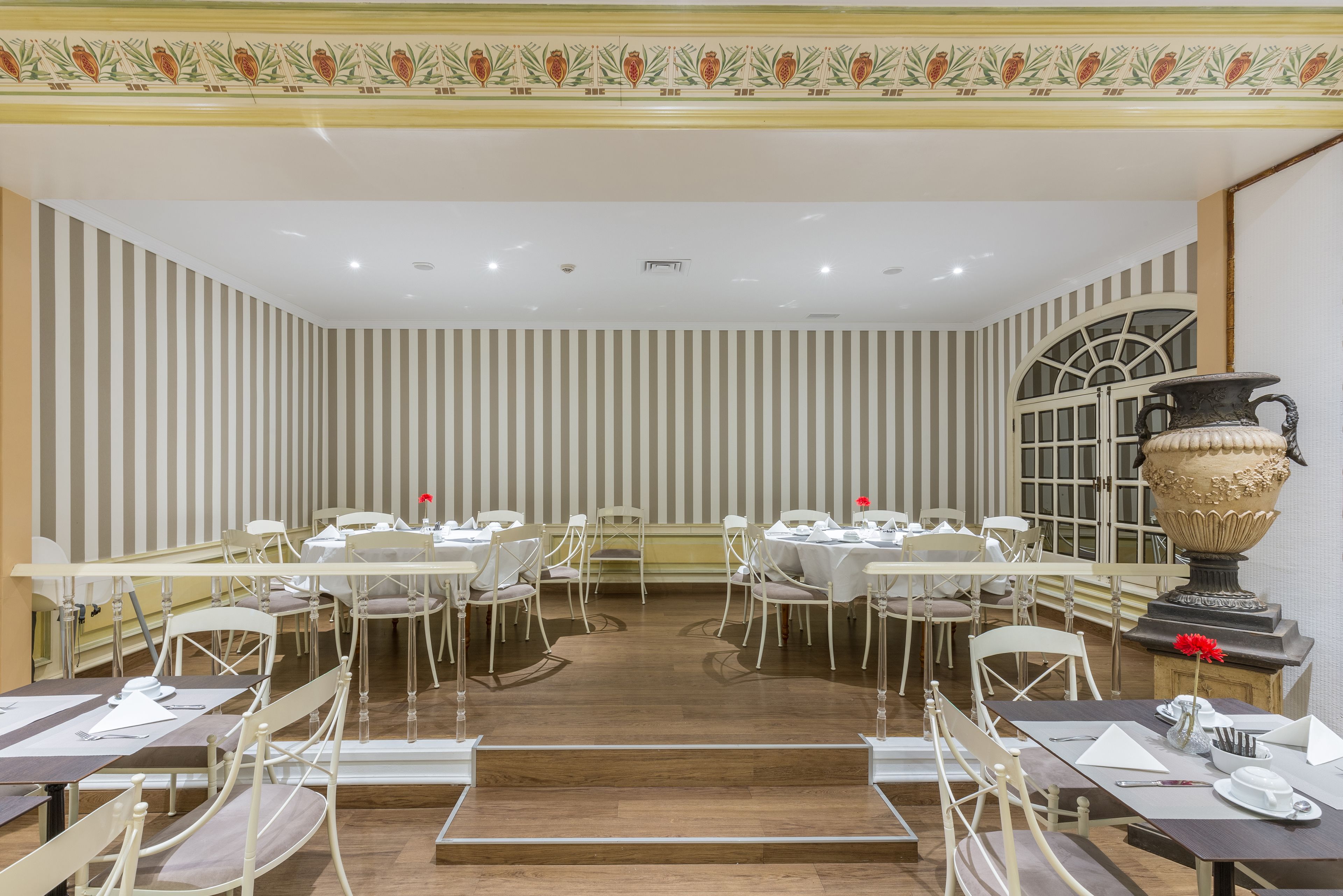 A dining area with striped wallpaper, white tables, and chairs.