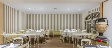A dining area with striped wallpaper, white tables, and chairs.