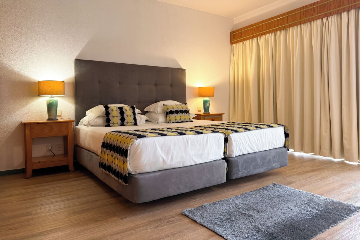 A double bed with a grey headboard, two bedside lamps, and a grey rug.