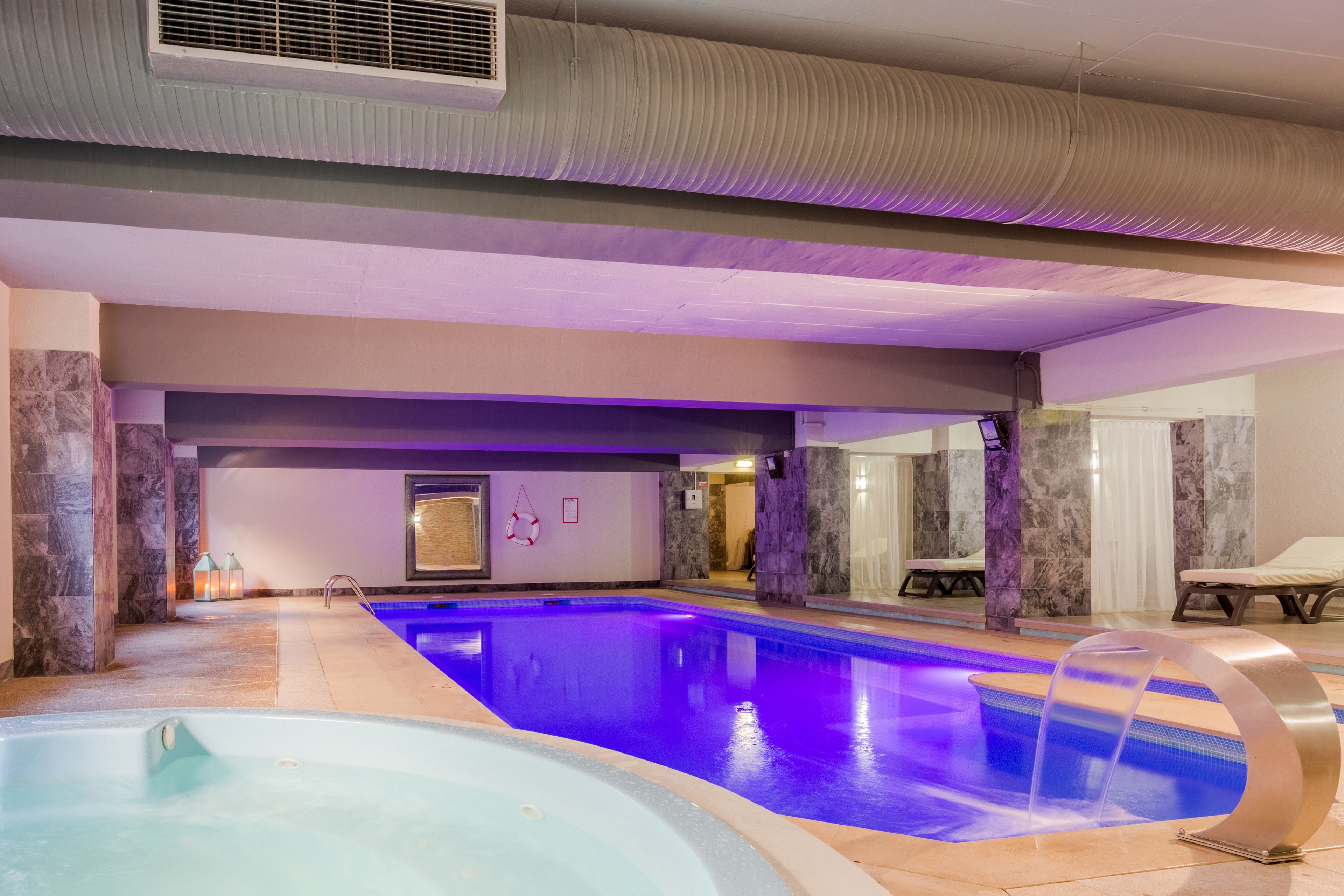 An indoor swimming pool with a blue-lit water feature, marble walls, and a ceiling with a textured design.