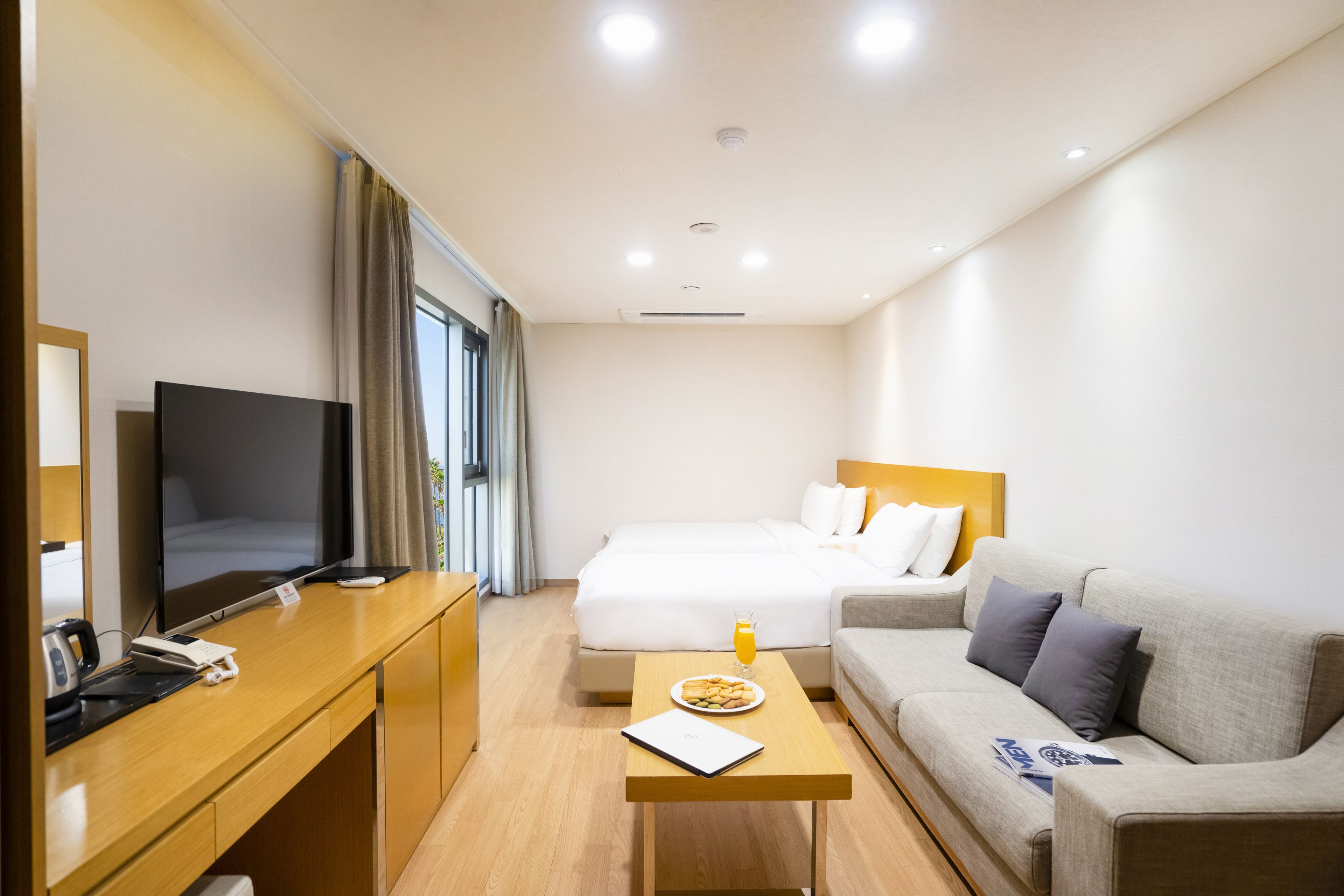 Een hotelkamer met een bed, een bank, een bureau met een televisie en een kleine tafel met eten erop.