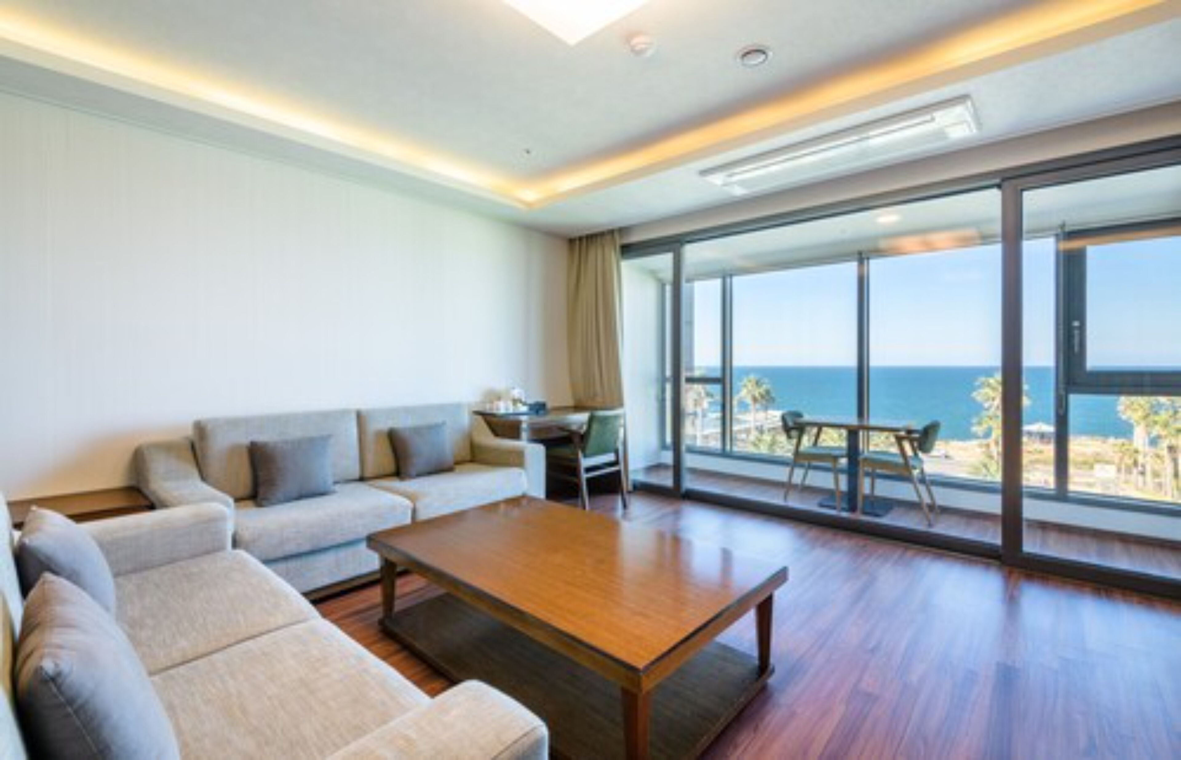 A modern living room with a sofa, coffee table, and a view of the ocean through large windows.