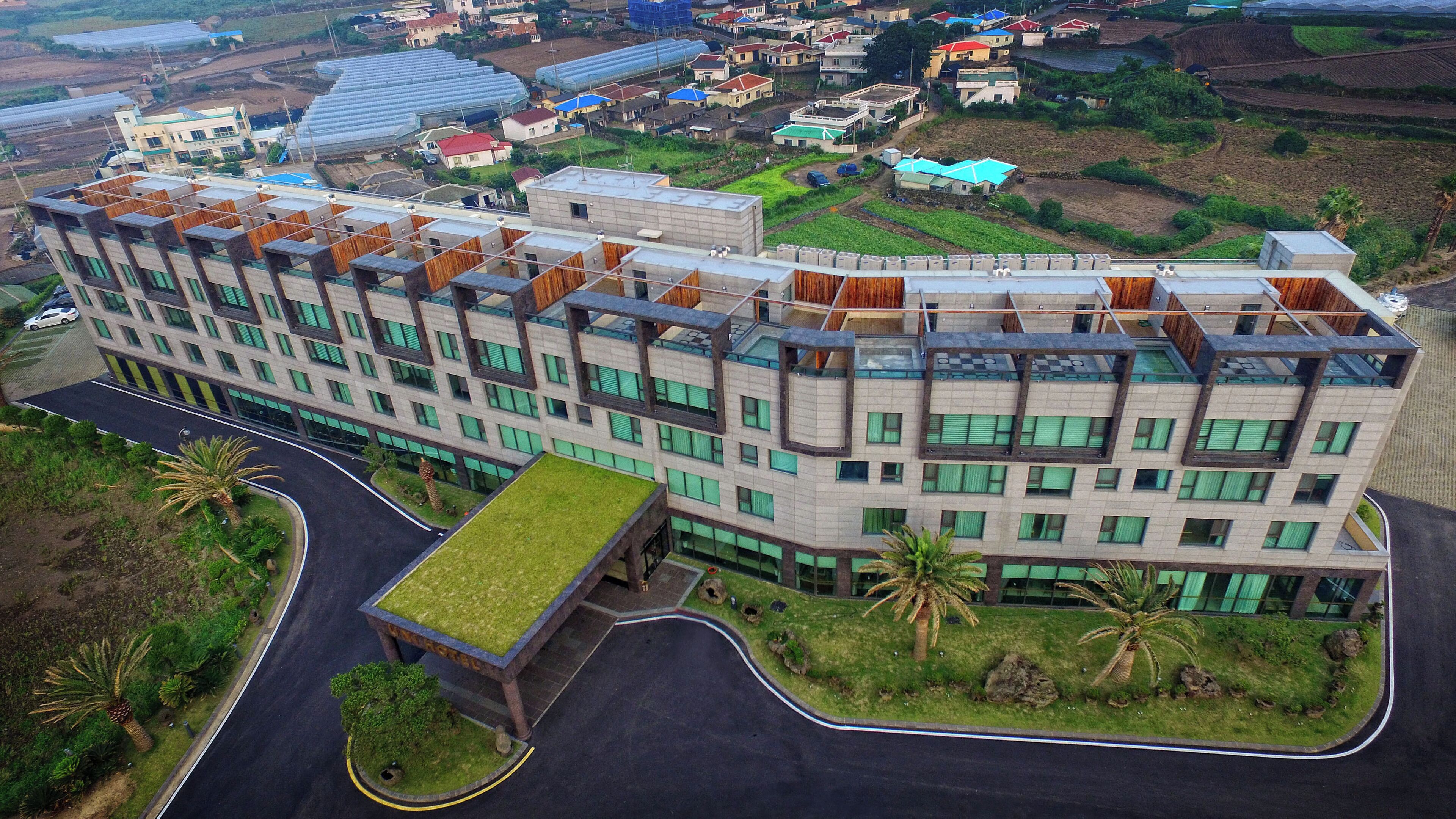 A modern hotel with a flat roof, multiple balconies, and a central courtyard with a grass lawn.