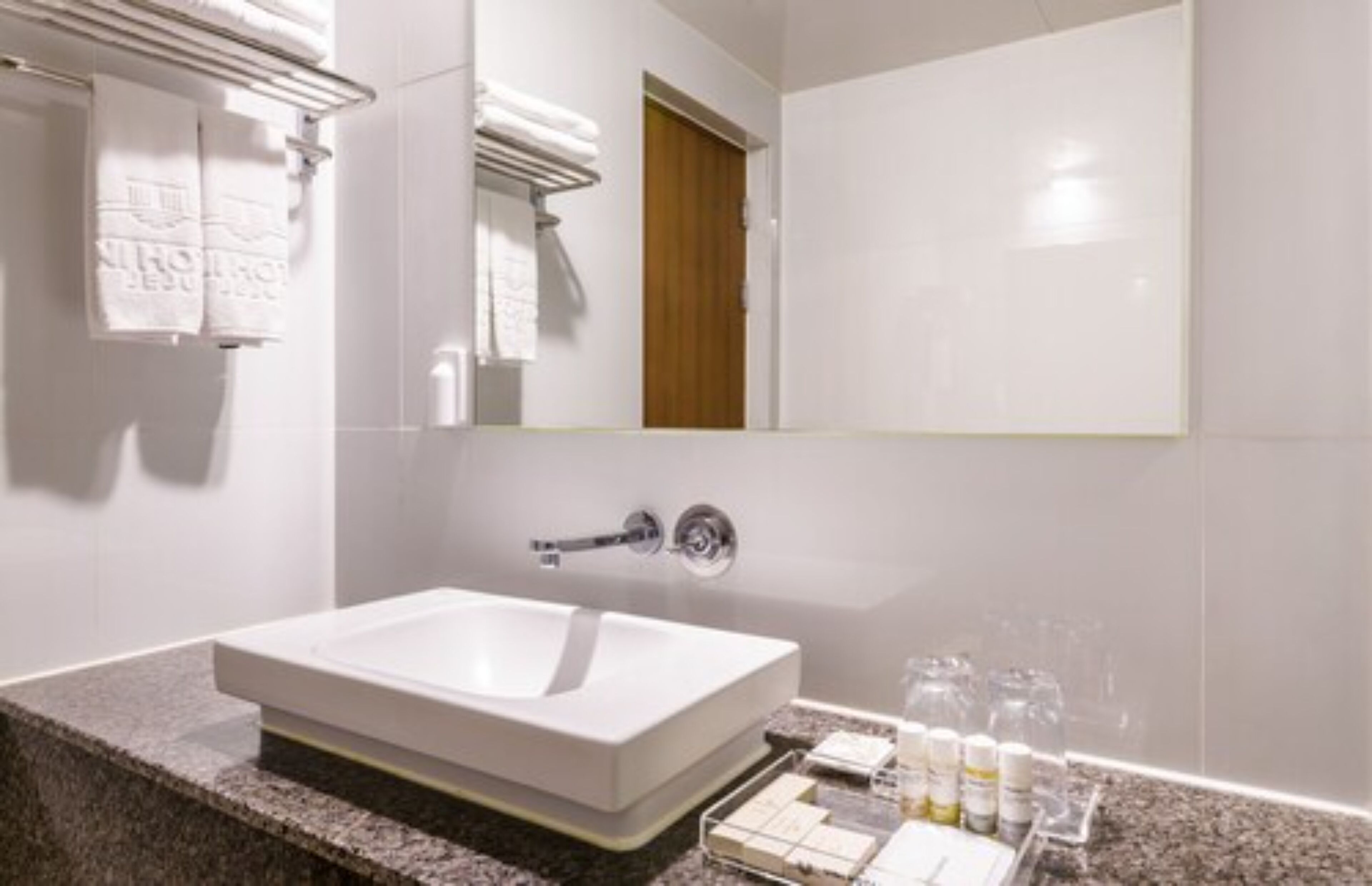 Un baño moderno con un lavamanos grande de color blanco, un espejo y una puerta de madera.