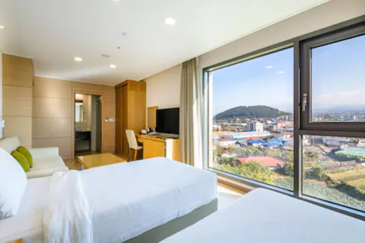 Une chambre d’hôtel avec une grande fenêtre, un lit, un bureau et une chaise.