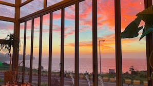 A room with large windows overlooking a coastal view, a seating area with a table and chairs, and a potted plant.