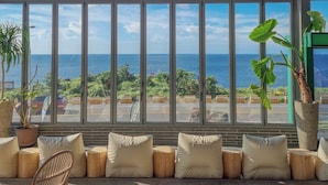 A seating area with a view of the ocean, large windows, and hanging wicker lamps.