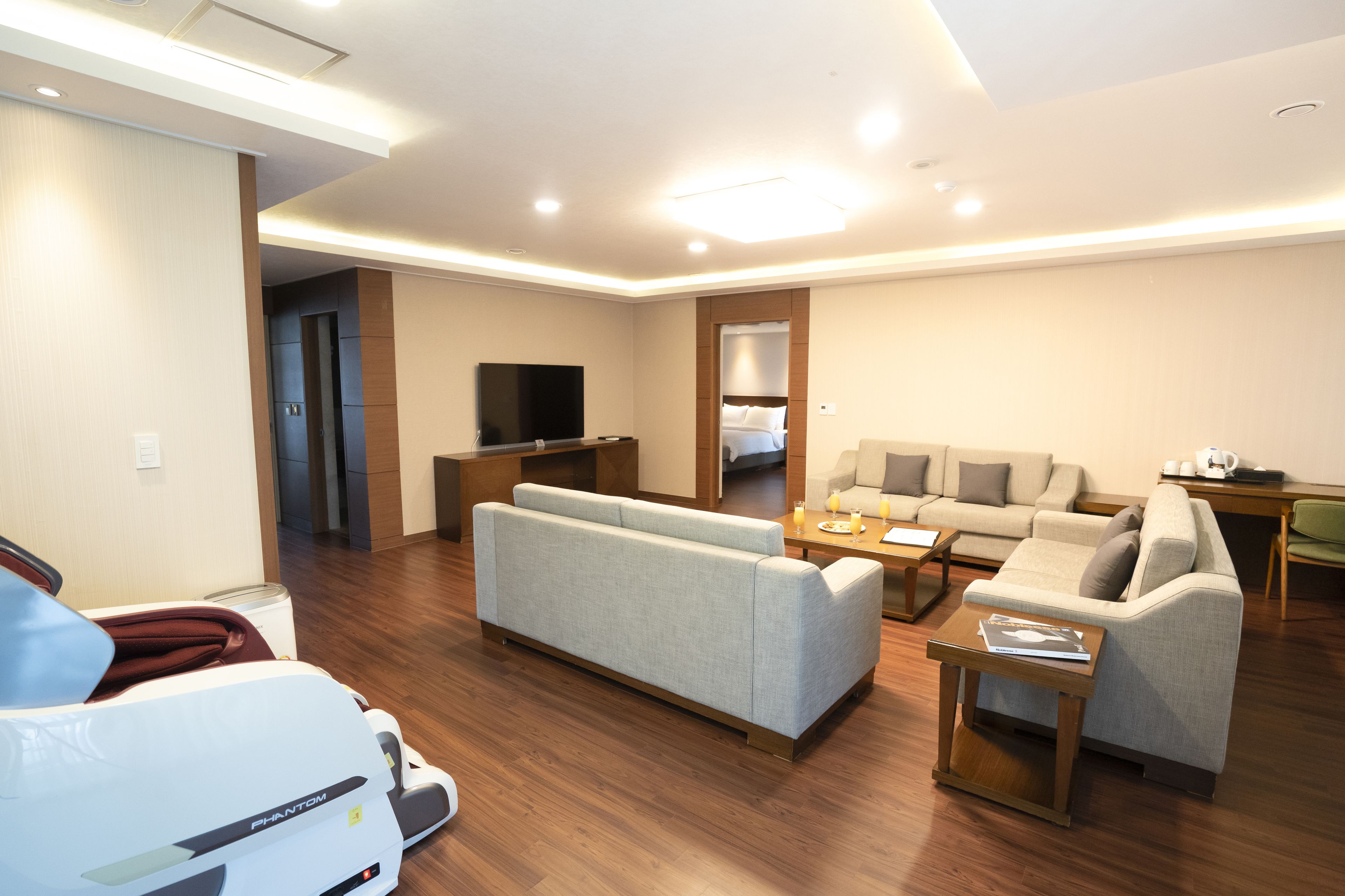 A modern living room with a sofa, a coffee table, and a TV. There is a wooden floor and a door leading to another room.