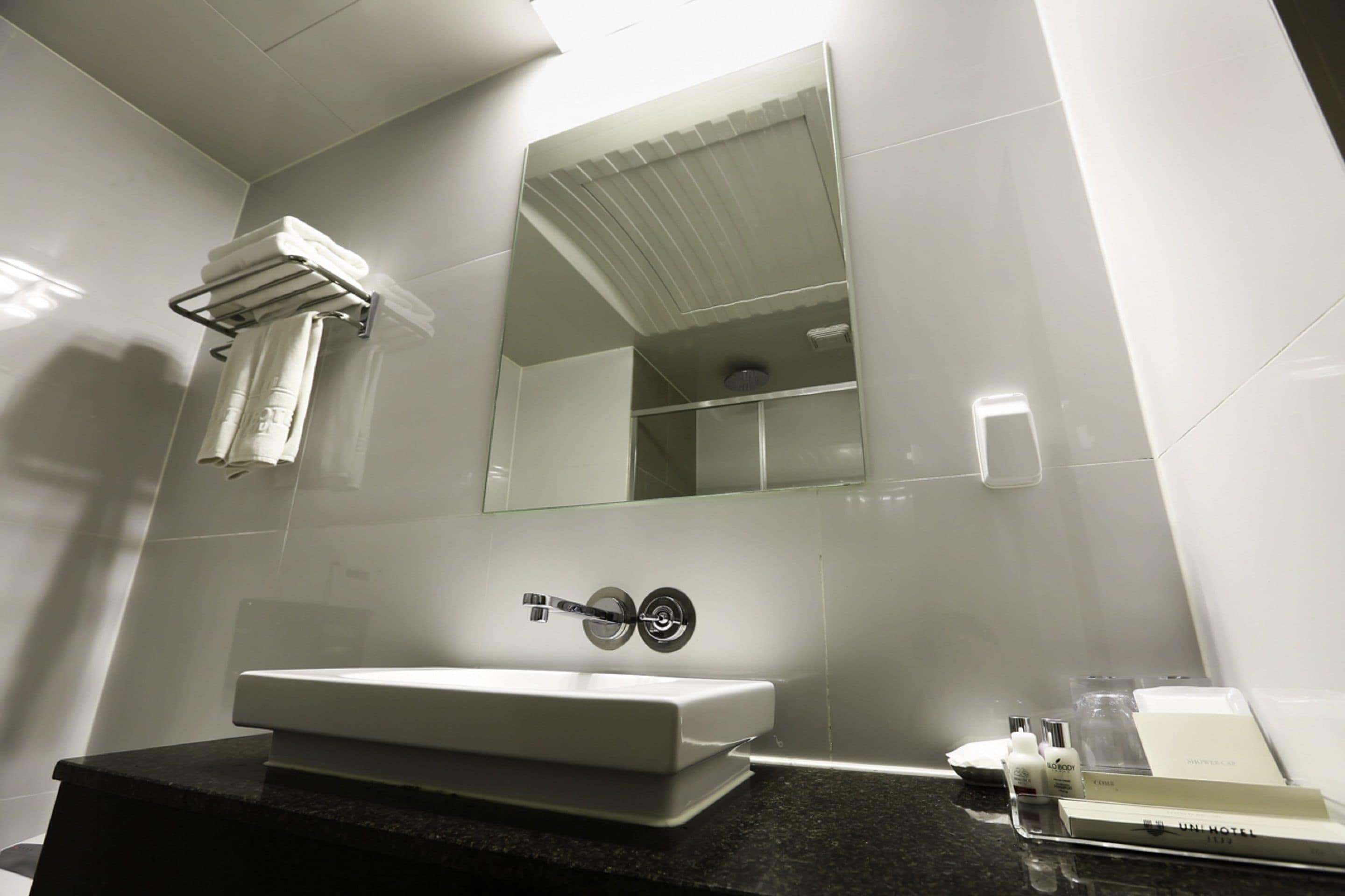 A modern bathroom with a white sink, a towel rack, a mirror, and toiletries on the counter.