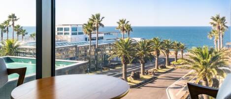 A balcony with a view of a pool, palm trees, and the ocean.