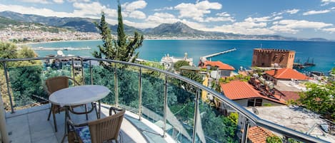 A balcony with a table and chairs overlooking a coastal cityscape with mountains in the background.