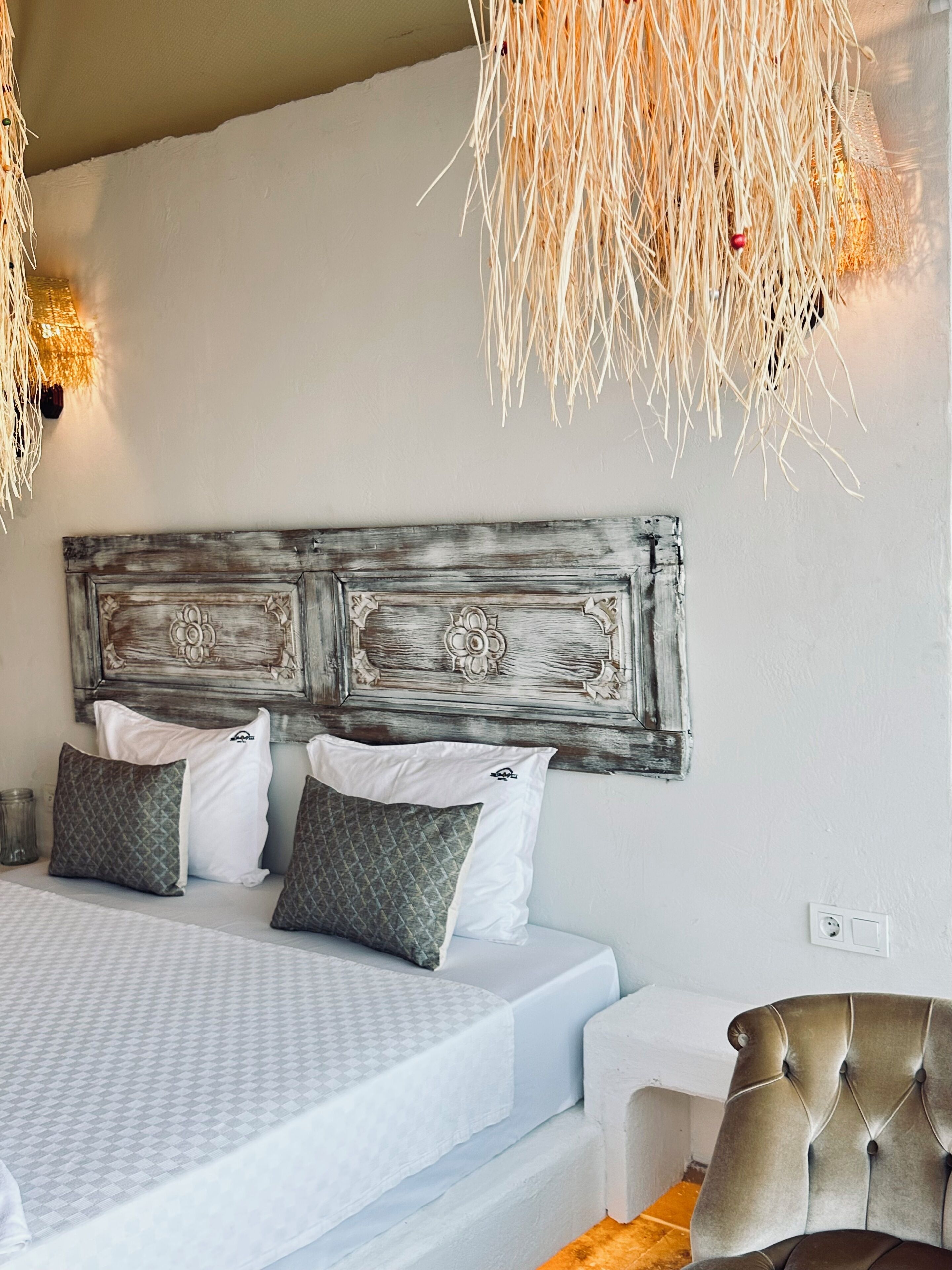 A bedroom with a large bed, a tufted armchair, and a rustic headboard.