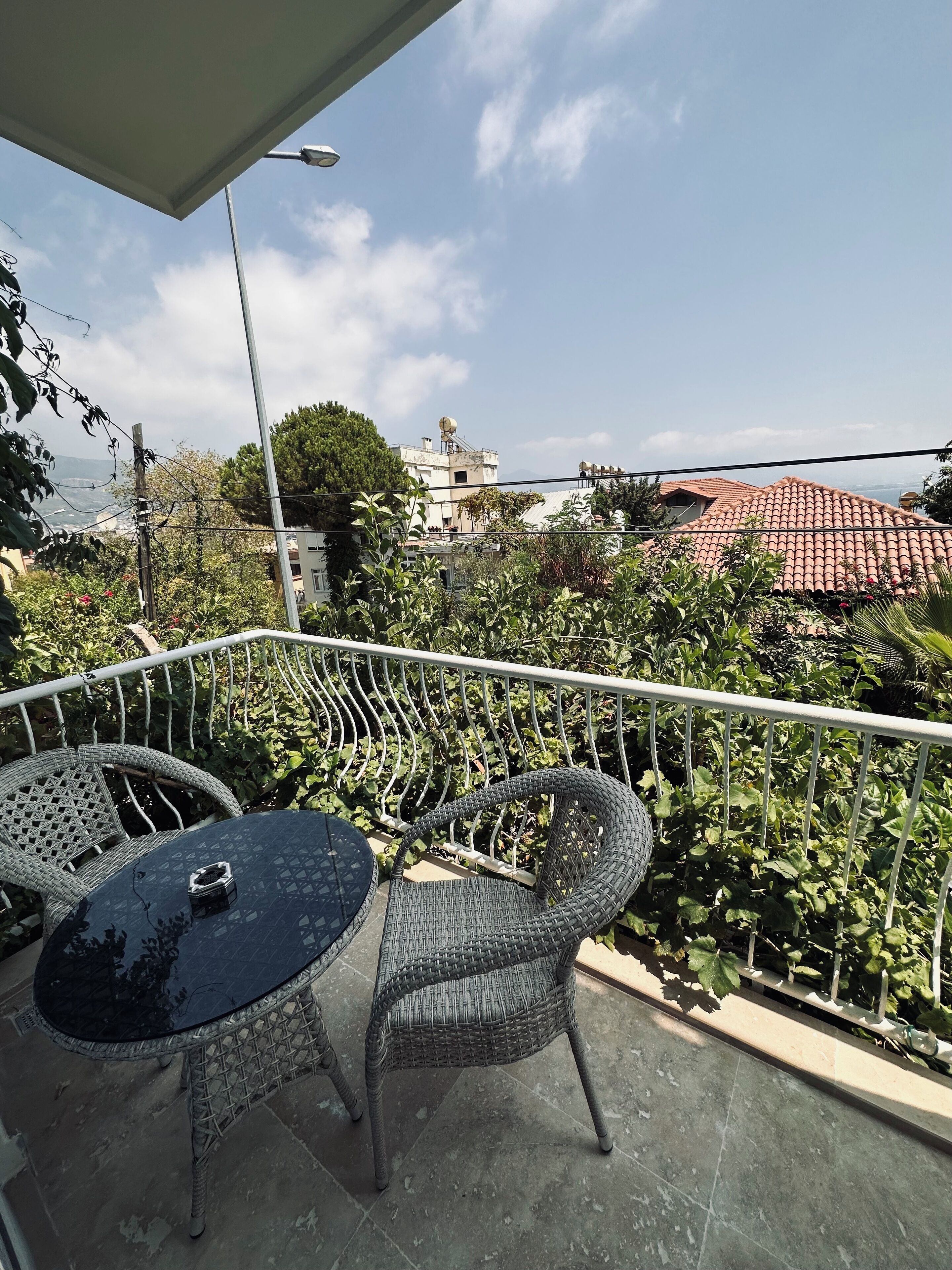 A balcony with a table and chairs, overlooking a residential area with red-tiled roofs and greenery.