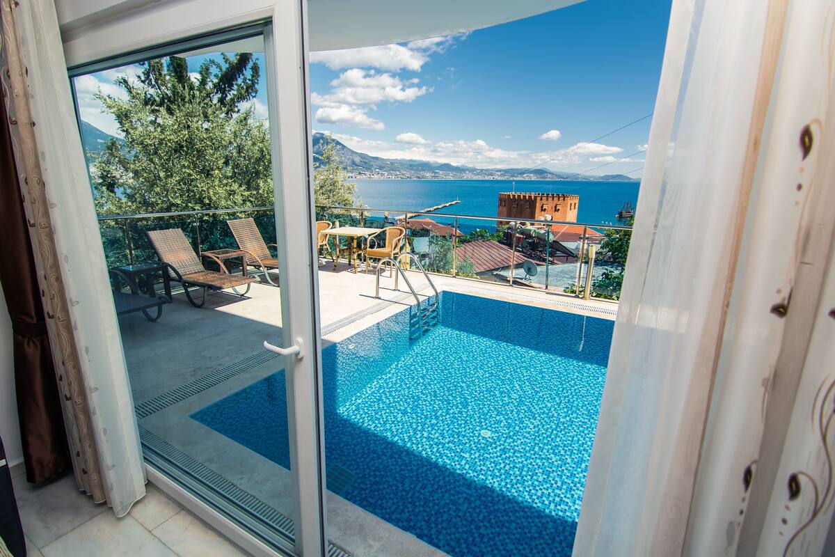 A balcony with a pool, overlooking a scenic view of the sea and mountains.