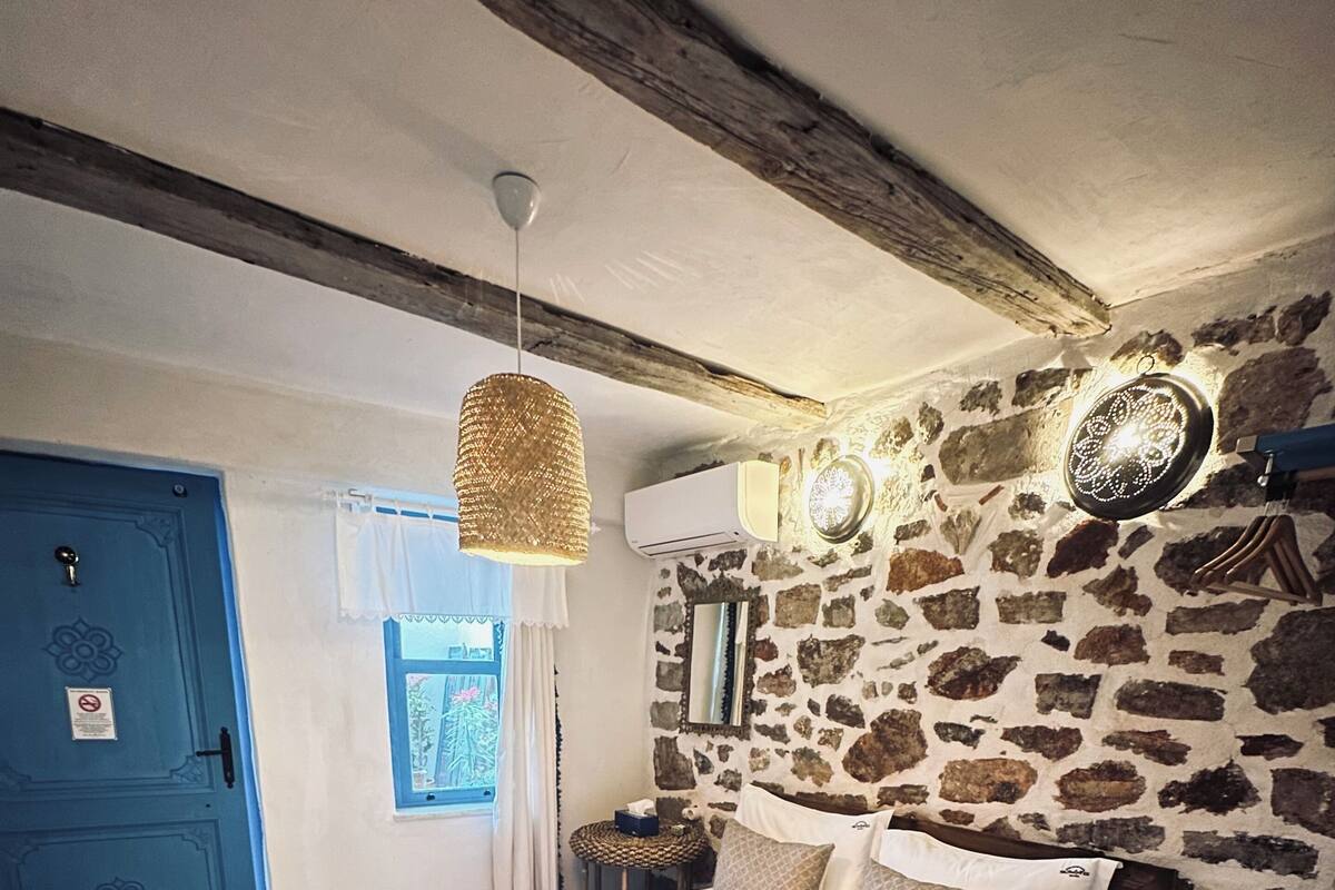 A bedroom with a stone wall, a bed with white bedding, a hanging light fixture, and a blue door.