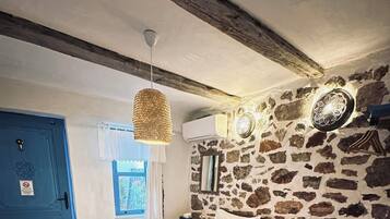 Une chambre avec un mur en pierre, un lit avec une literie blanche, un luminaire suspendu et une porte bleue.