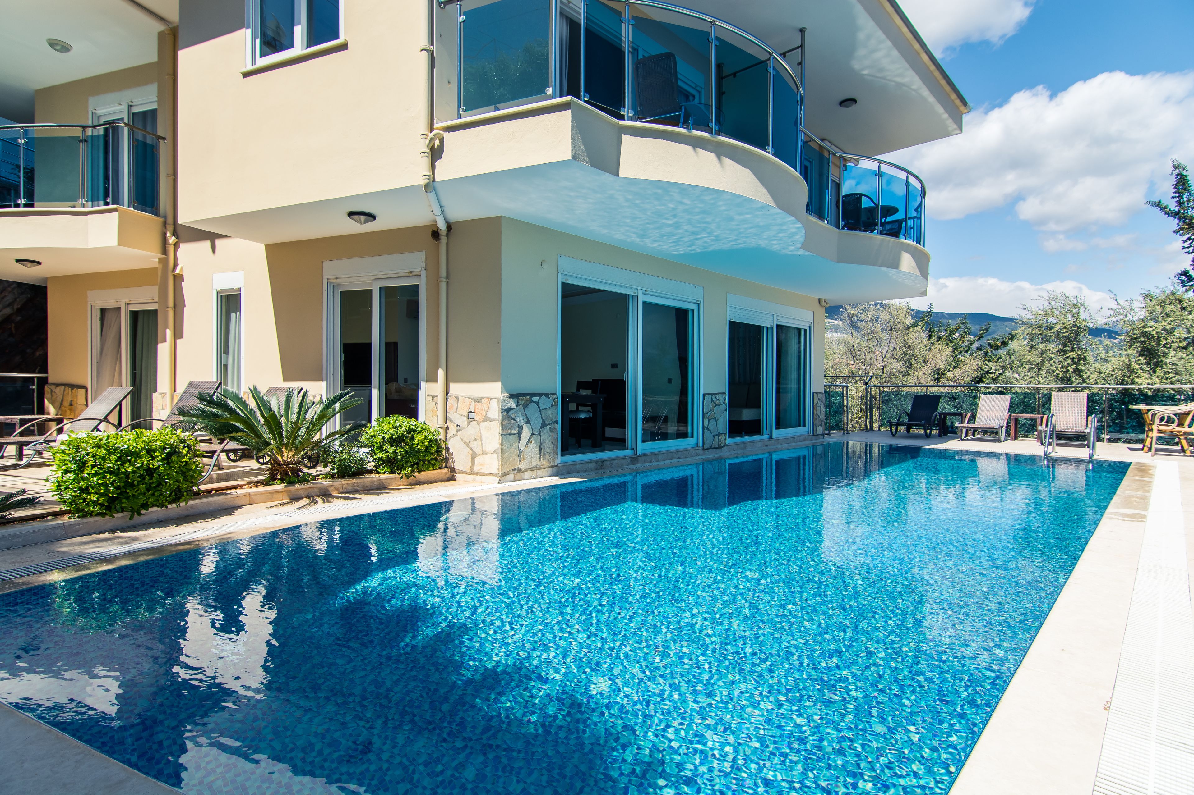 A modern two-story house with a swimming pool, large windows, and outdoor furniture.
