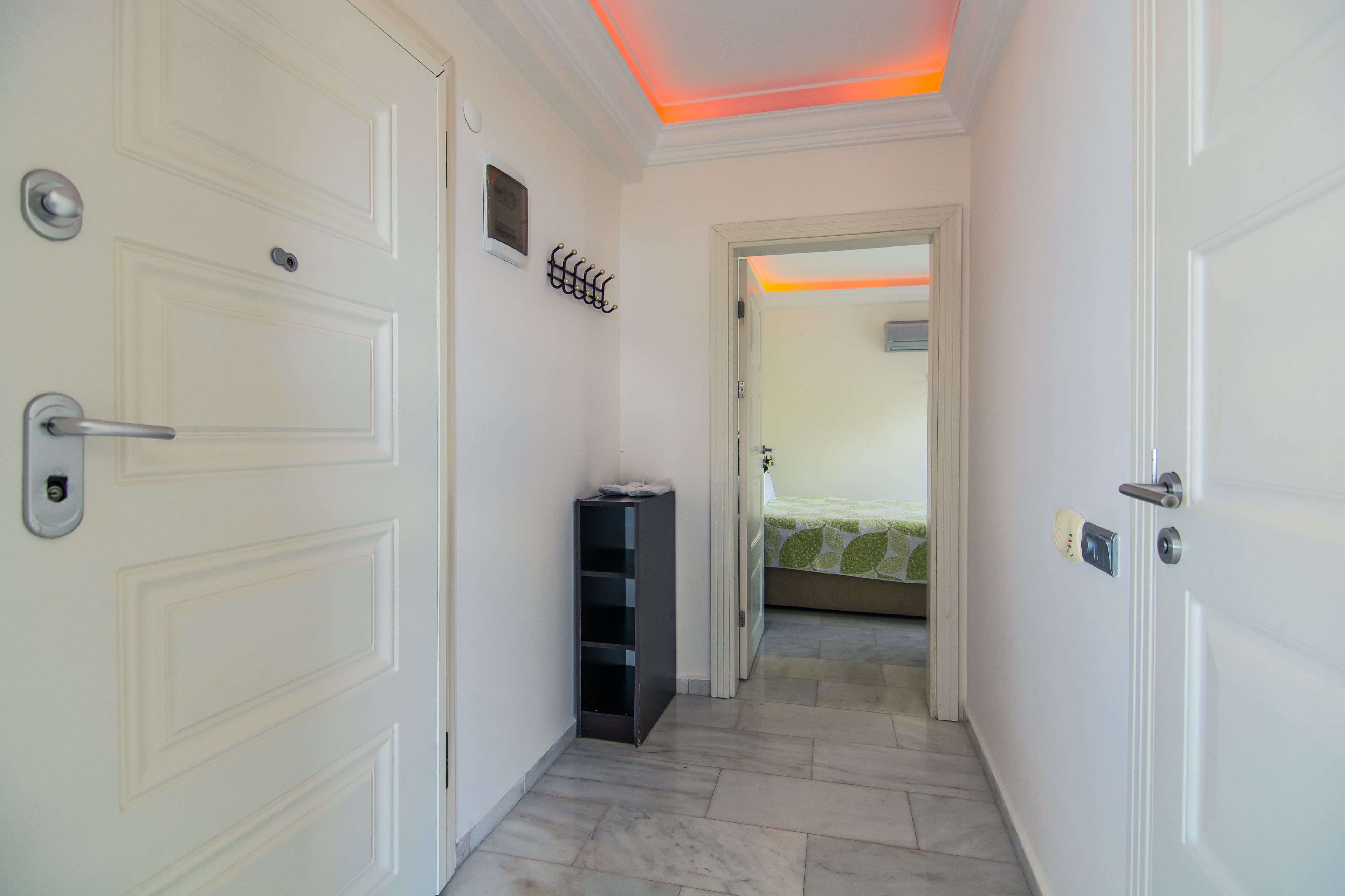 A hallway with white doors, a small black cabinet, and a bed with a green and white bedspread in the background.