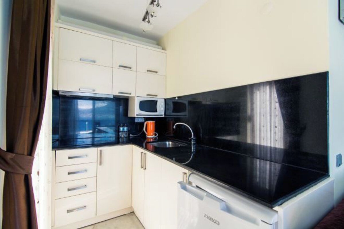 A compact kitchen with white cabinets, a black countertop, a microwave, a sink, and a dishwasher.