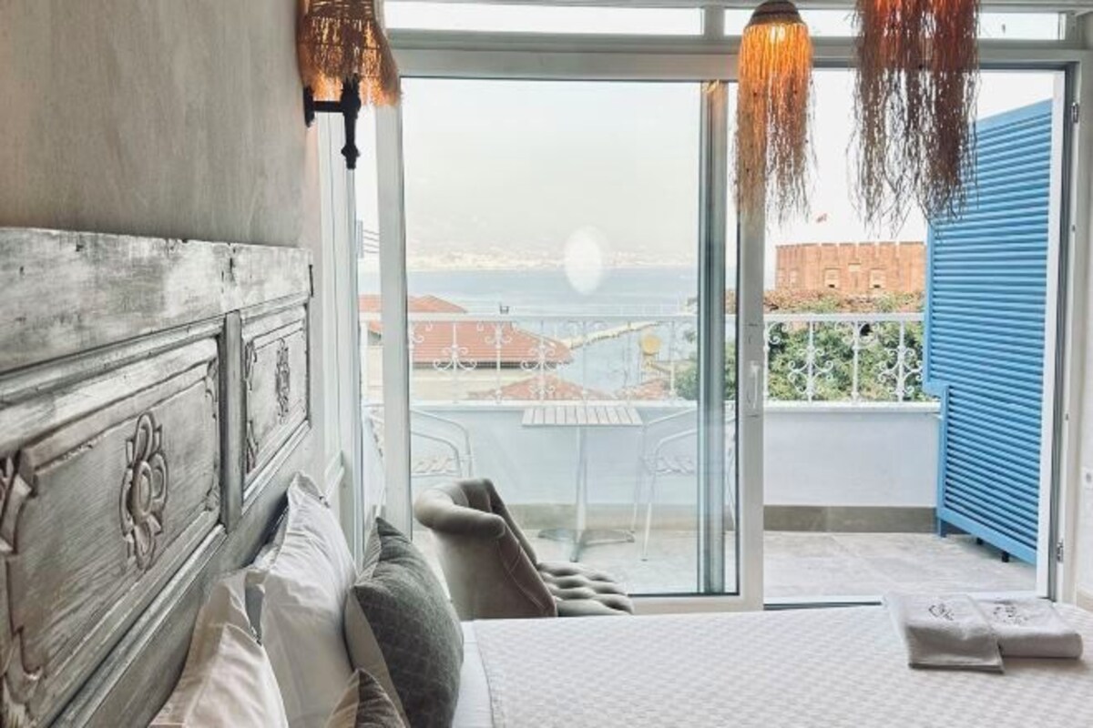 A bedroom with a large bed, a view of the sea, and a balcony with a table and chairs.