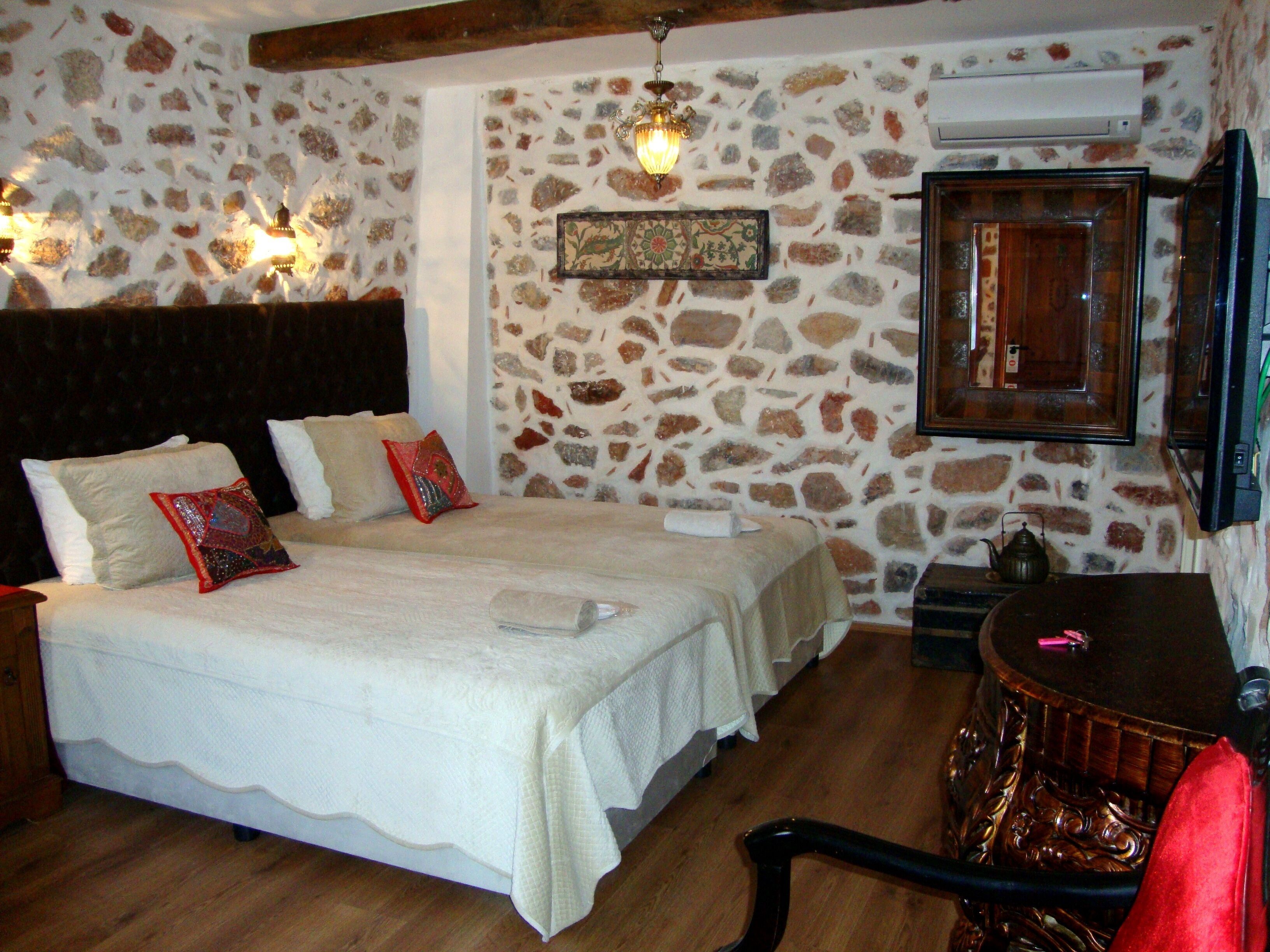 A bedroom with a stone wall, a bed with white bedding, a wooden headboard, and a small table with a teapot.