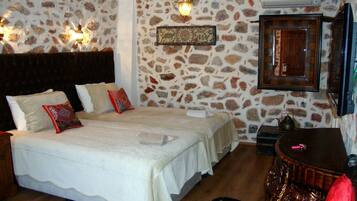 A bedroom with a stone wall, a bed with white bedding, a wooden headboard, and a small table with a teapot.