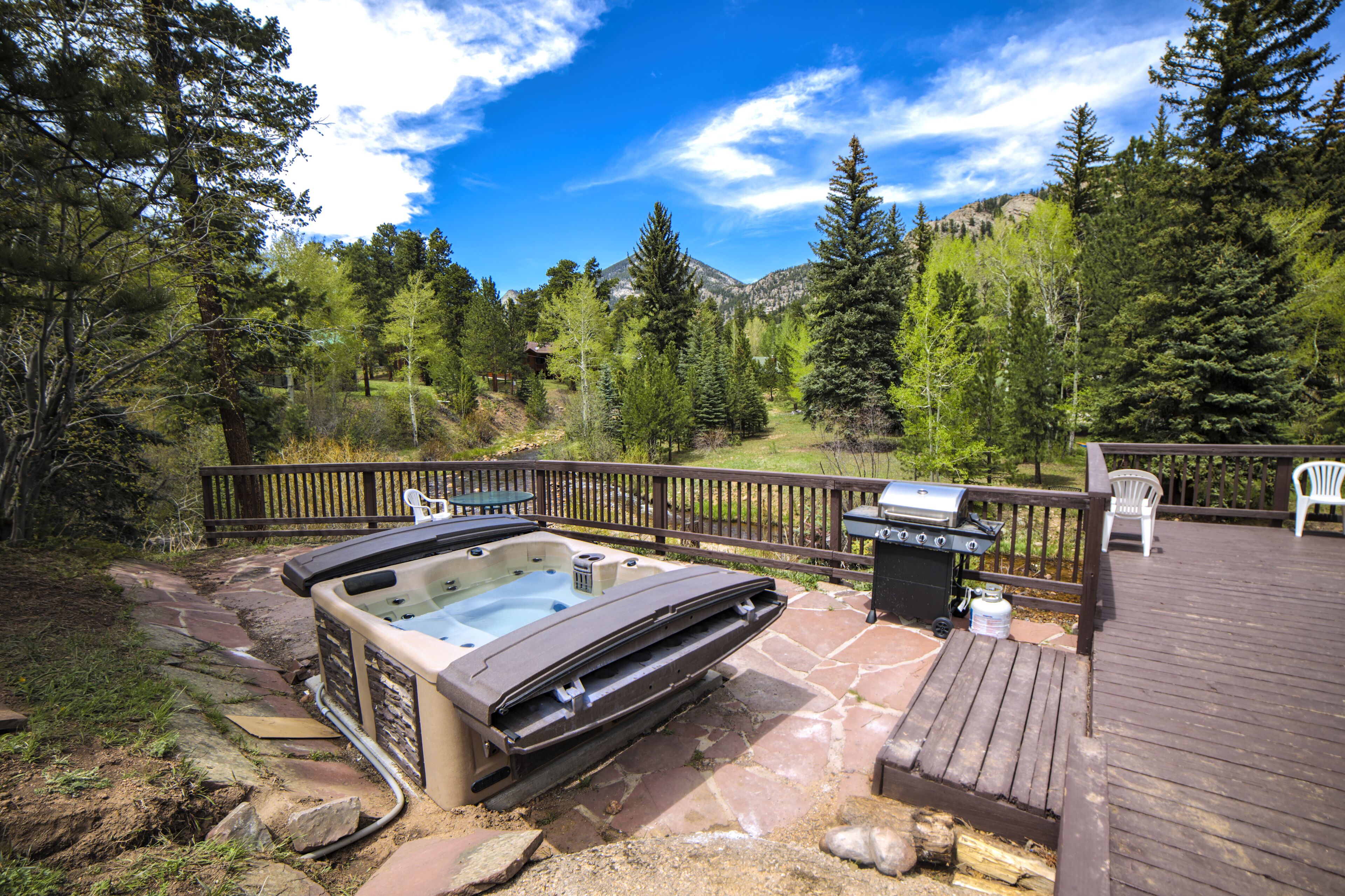 A hot tub on a stone deck with a barbecue grill and patio furniture.