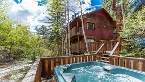 Een houten chalet met een jacuzzi en een terras dat uitkijkt over een bebost gebied.