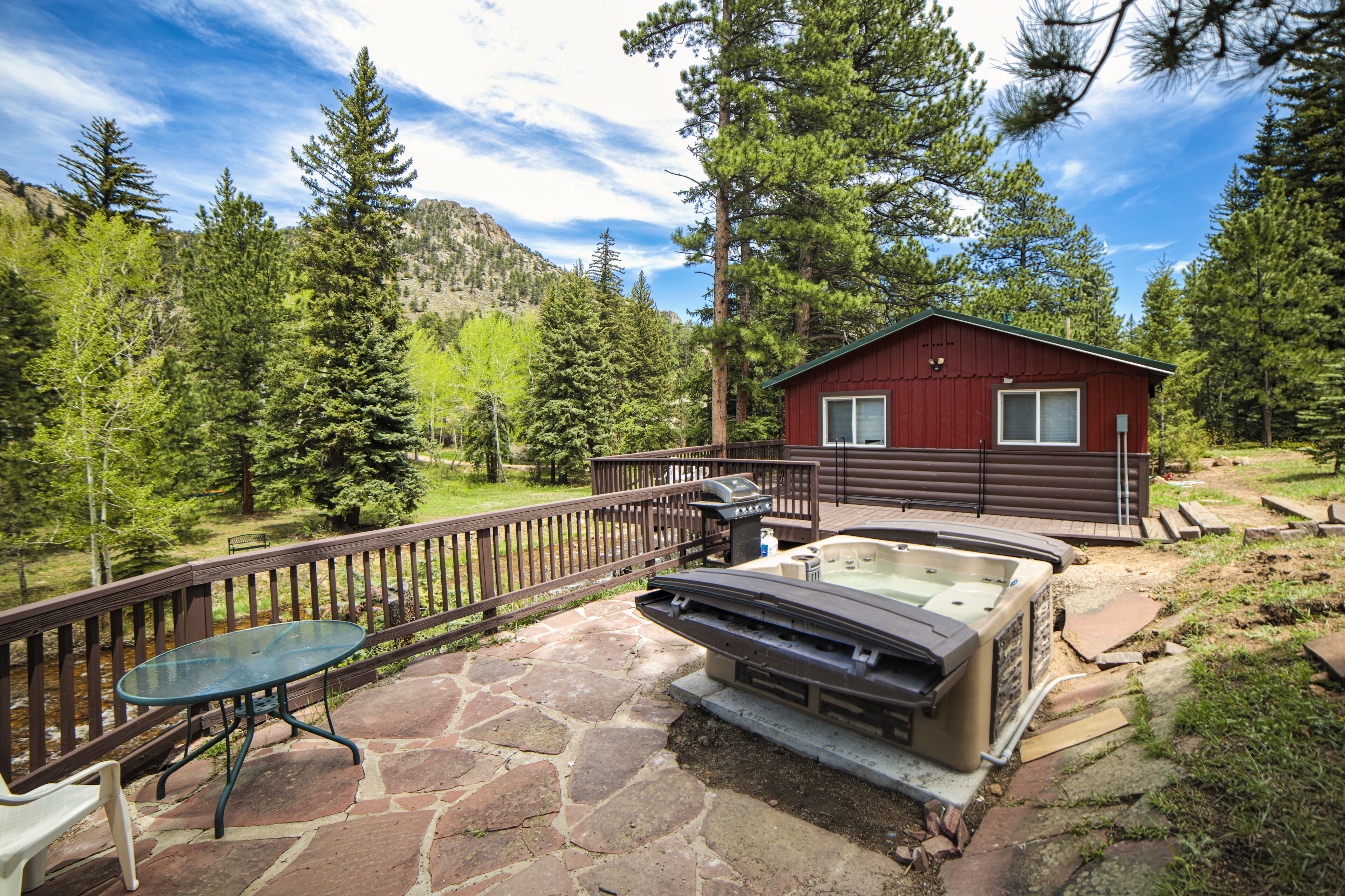 Una cabaña con jacuzzi, patio de piedra y terraza con vistas a un bosque.