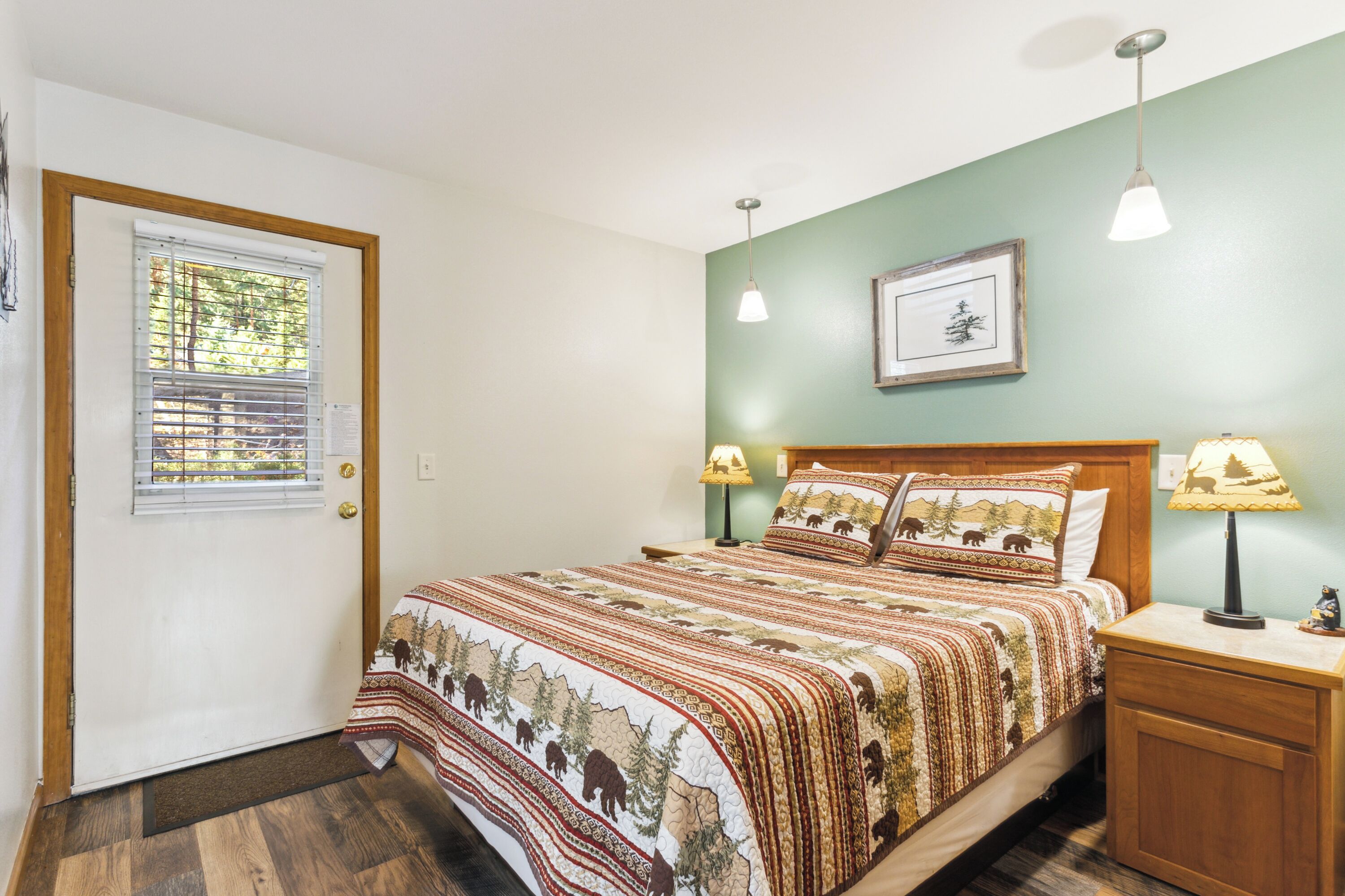 Une chambre à coucher avec un grand lit, deux lampes de chevet, une table de nuit, une porte avec des stores et un tableau encadré au mur.
