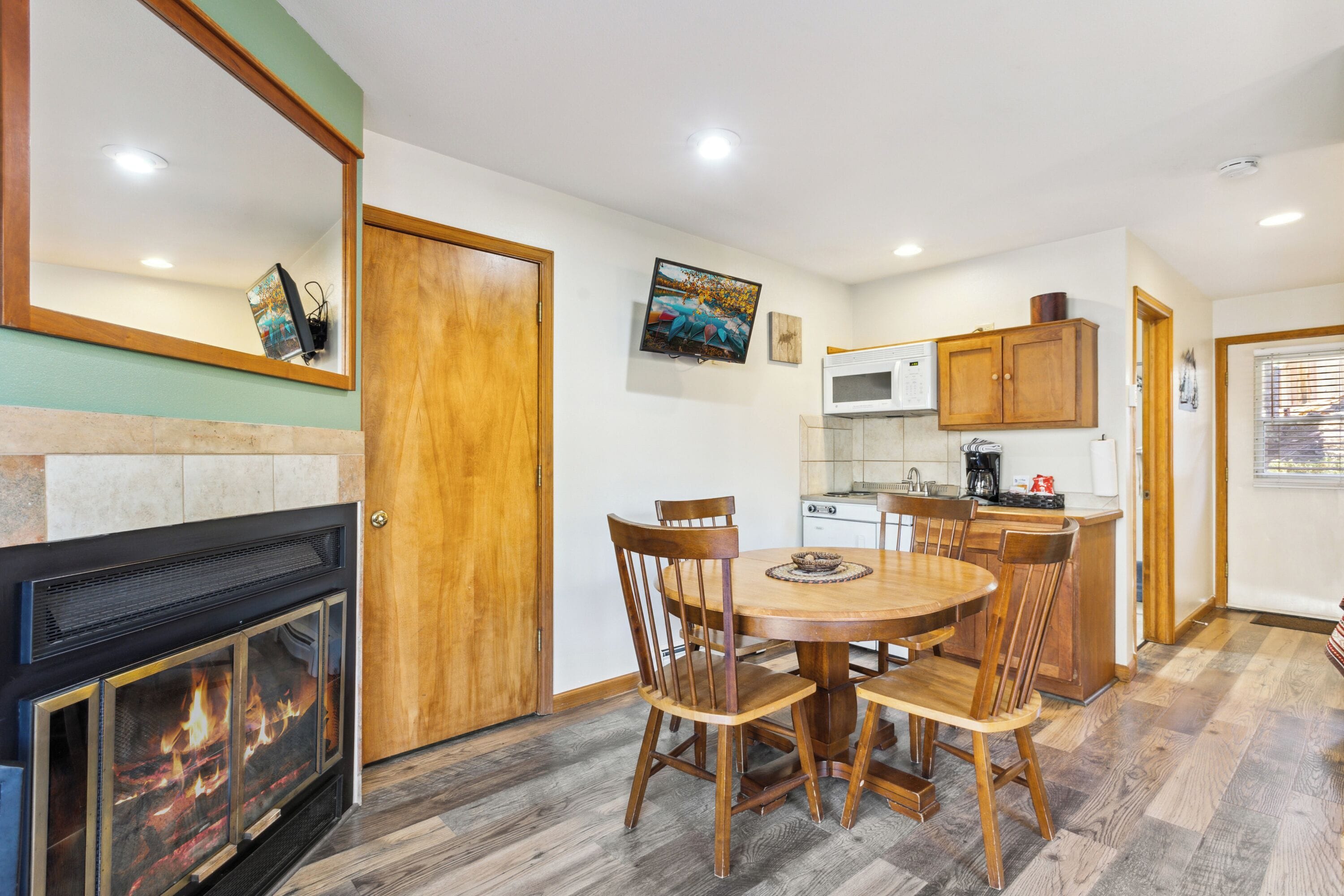 A dining area with a fireplace, wooden chairs, a round table, and a kitchen with a microwave and cabinets.