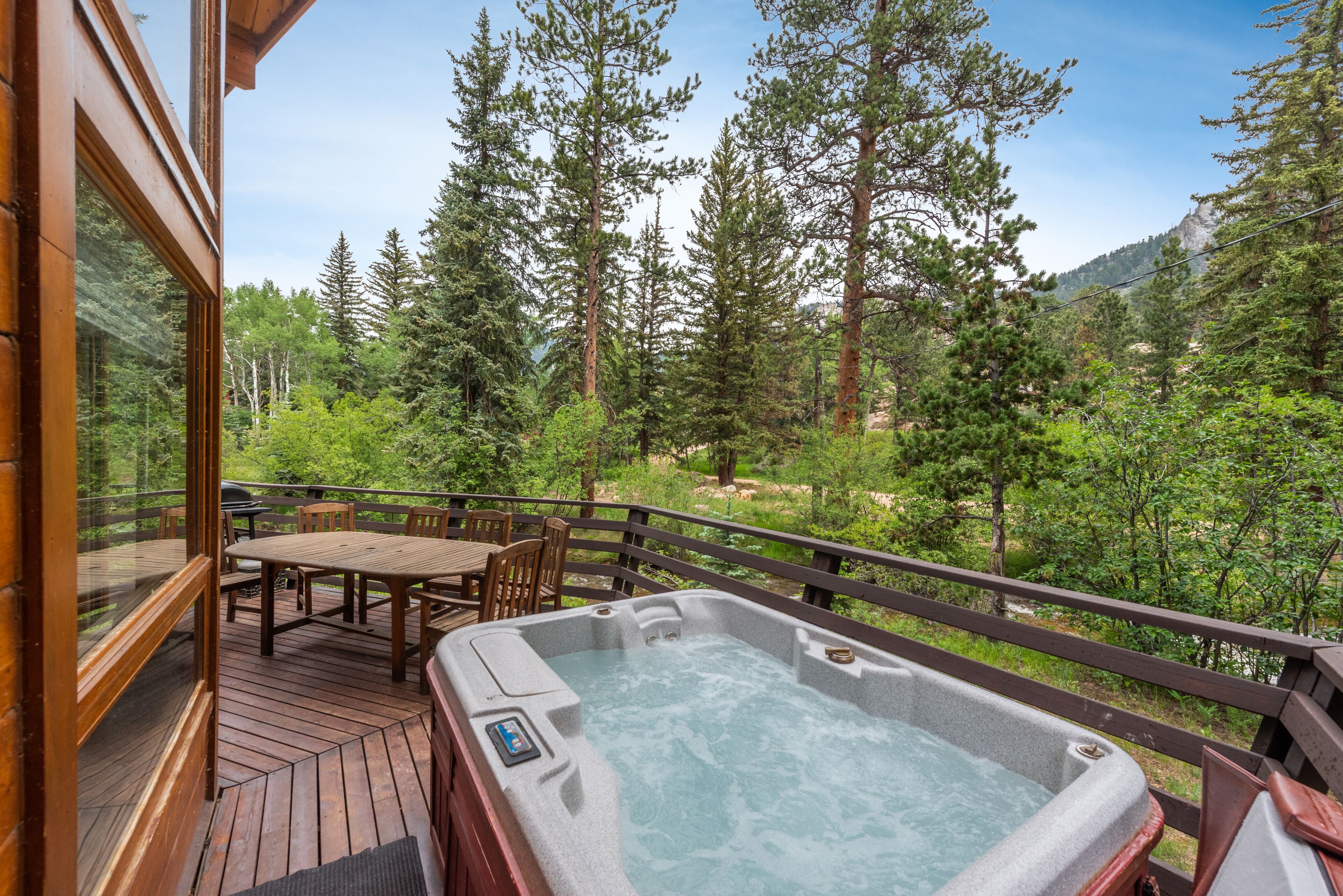 Een houten terras met een jacuzzi, houten meubels en uitzicht op een bebost gebied.