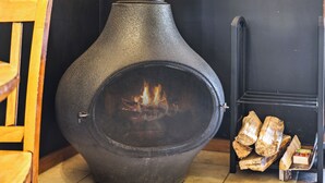 Een houtkachel met schoorsteen, een stoel en een stapel hout.