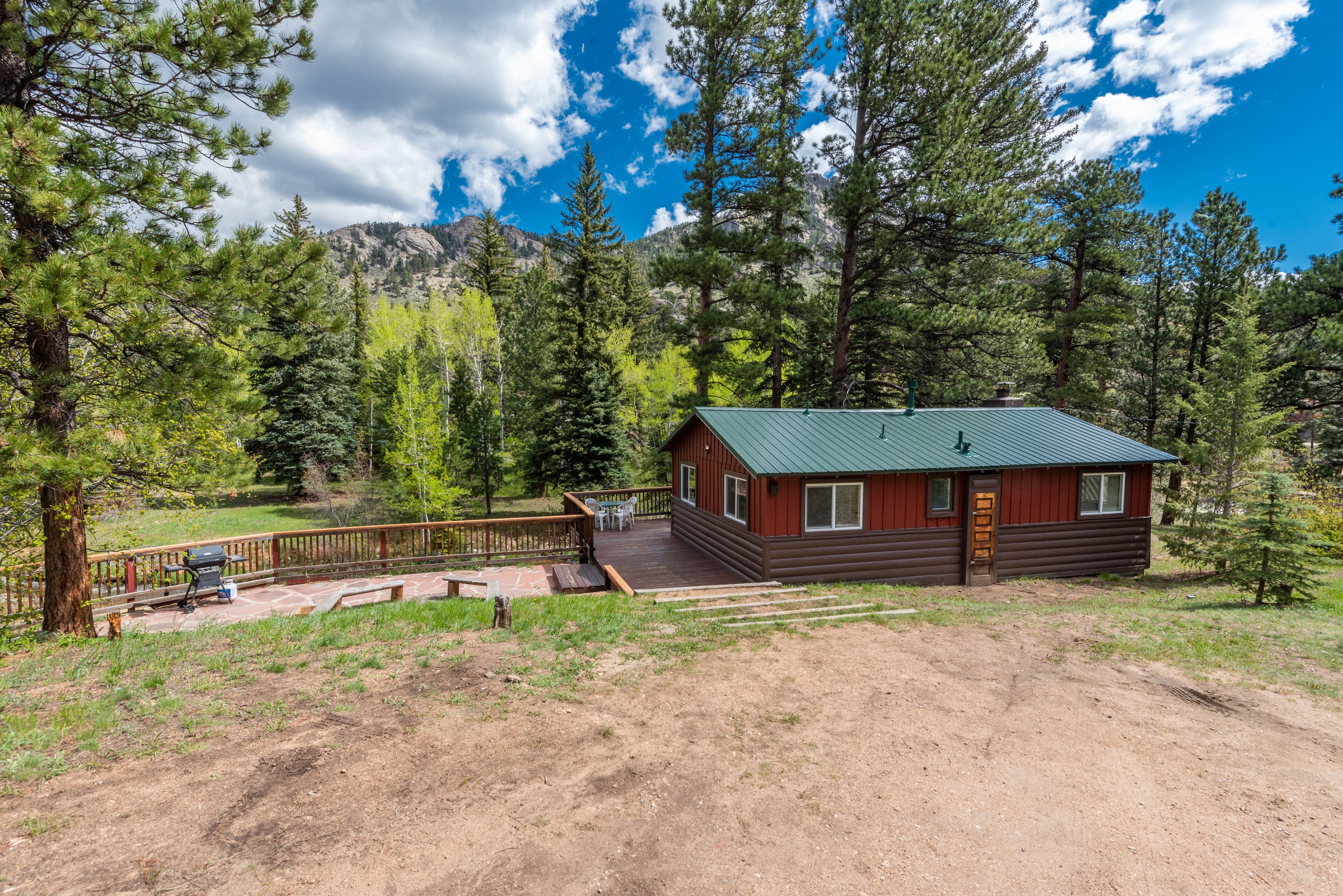 A cabin with a green roof, wooden deck, and a dirt path leading to it.