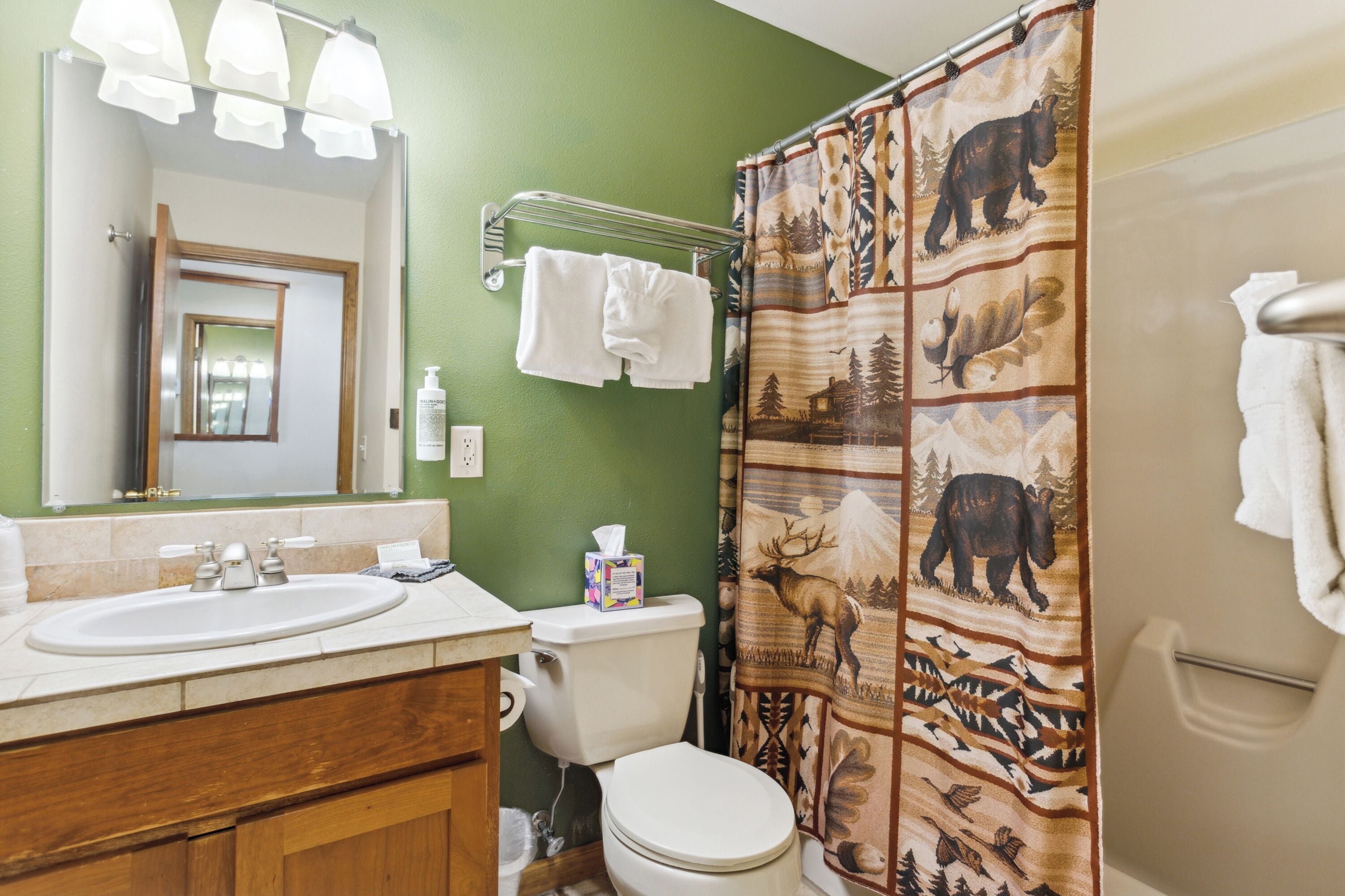 Een badkamer met een groene wand, een wit wastafelmeubel, een toilet en een douchegordijn met een dierenprint.