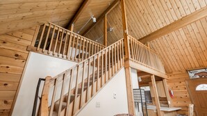 Een houten interieur met een trap naar een vide, een bank en een bordje met de tekst 'Welcome Cabin'.