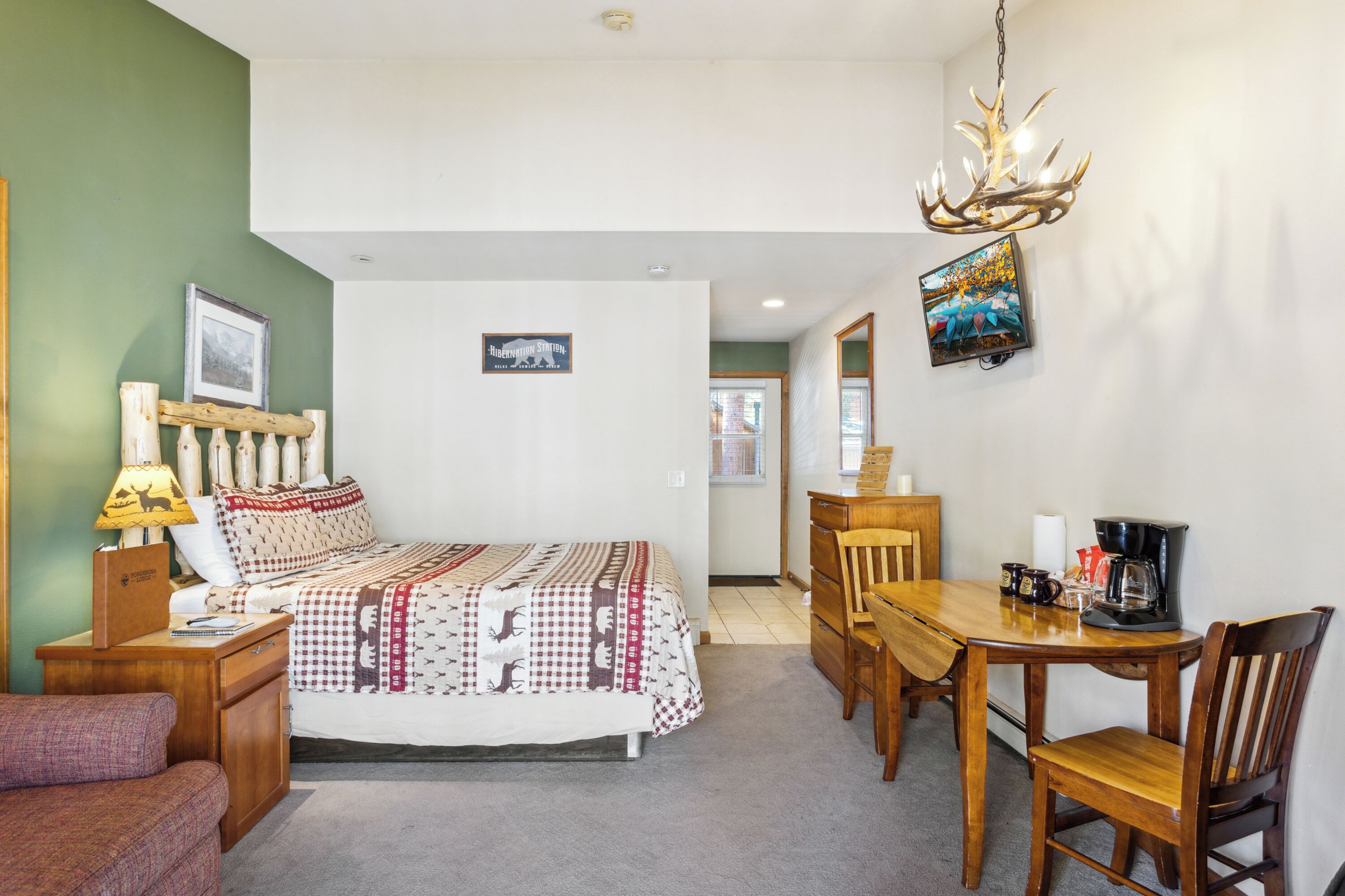 A bedroom with a bed, a desk, a chair, a lamp, and a television.