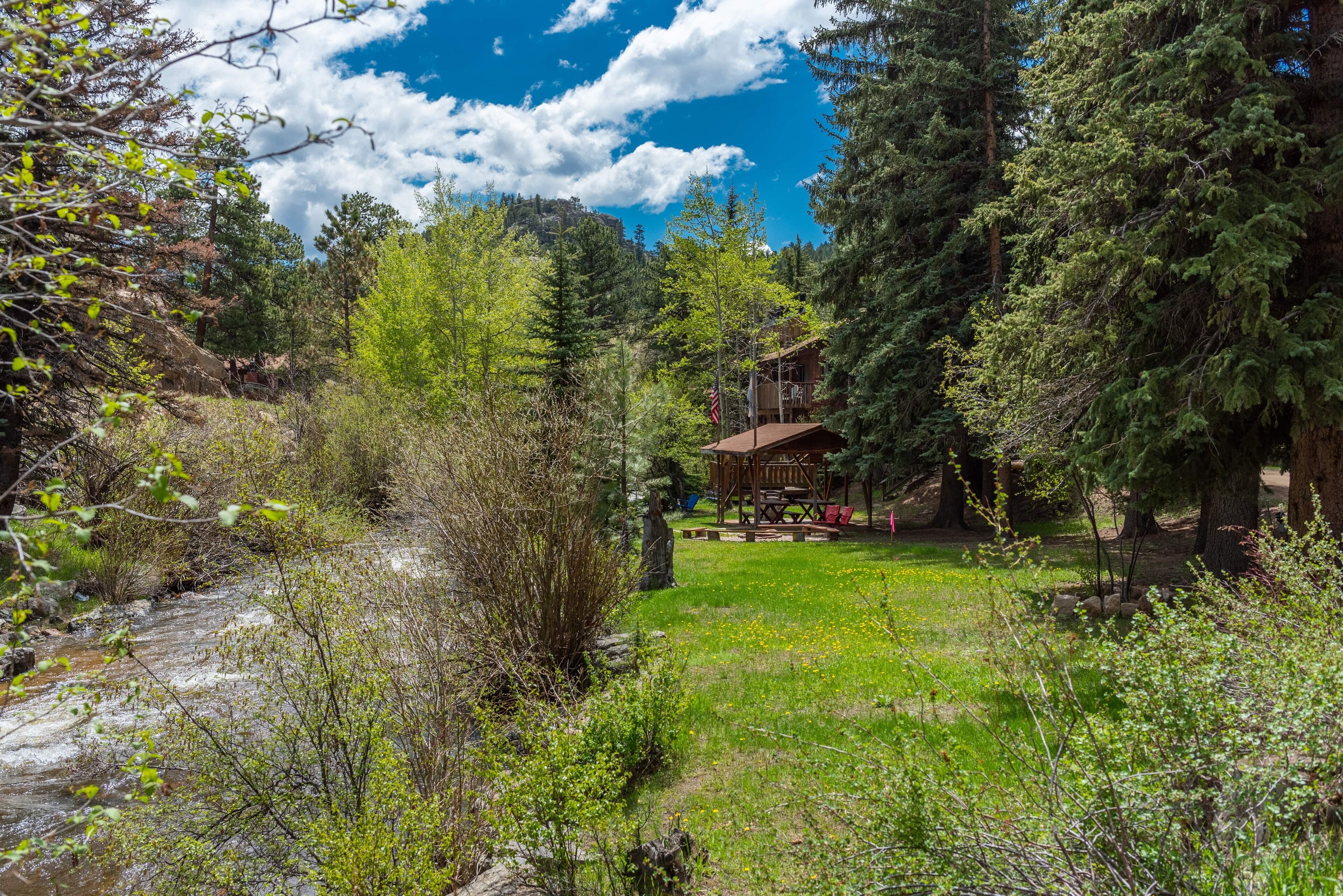 A cabin with a deck overlooking a forested area and a stream.