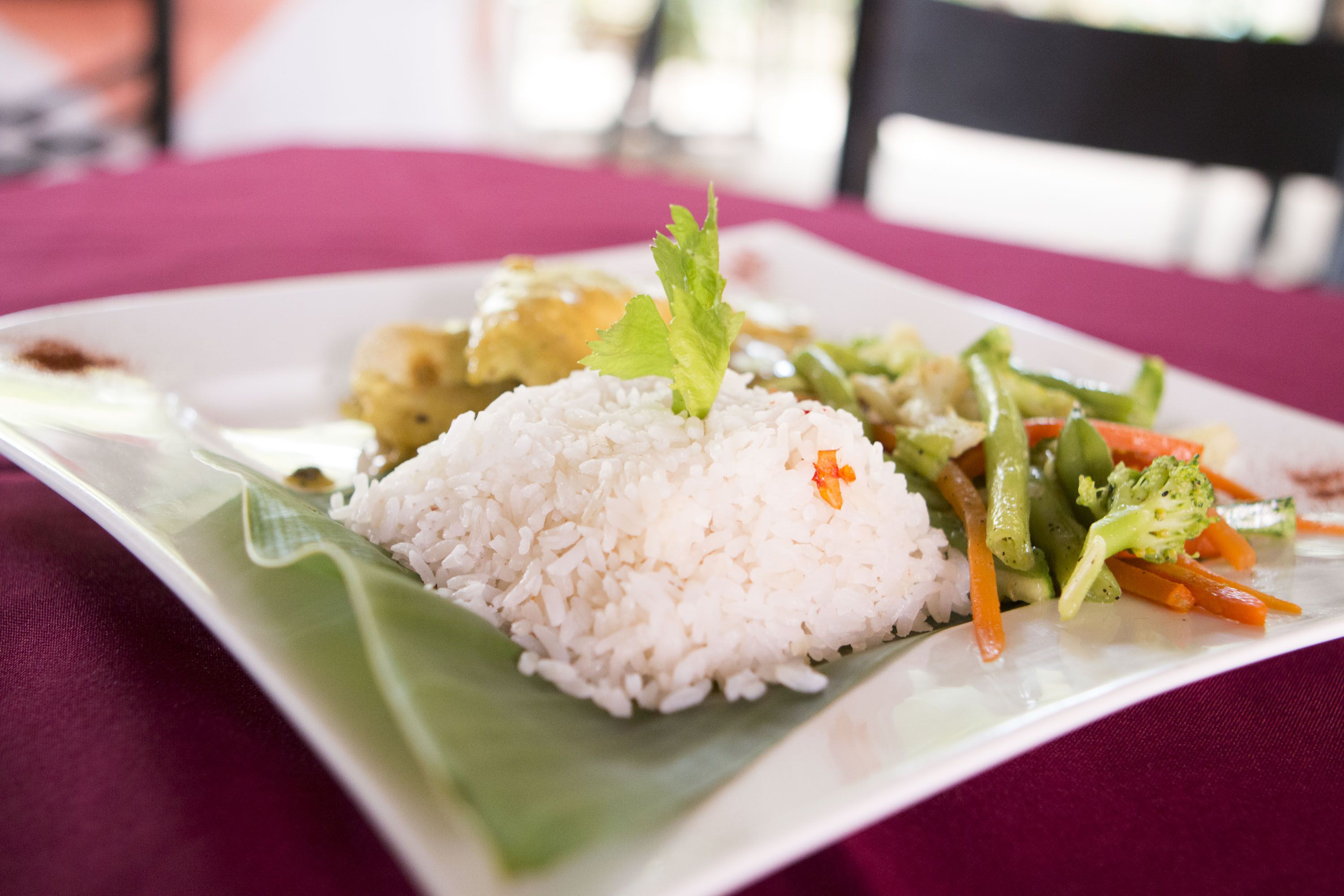 A plate of white rice with vegetables and a garnish on a square plate.