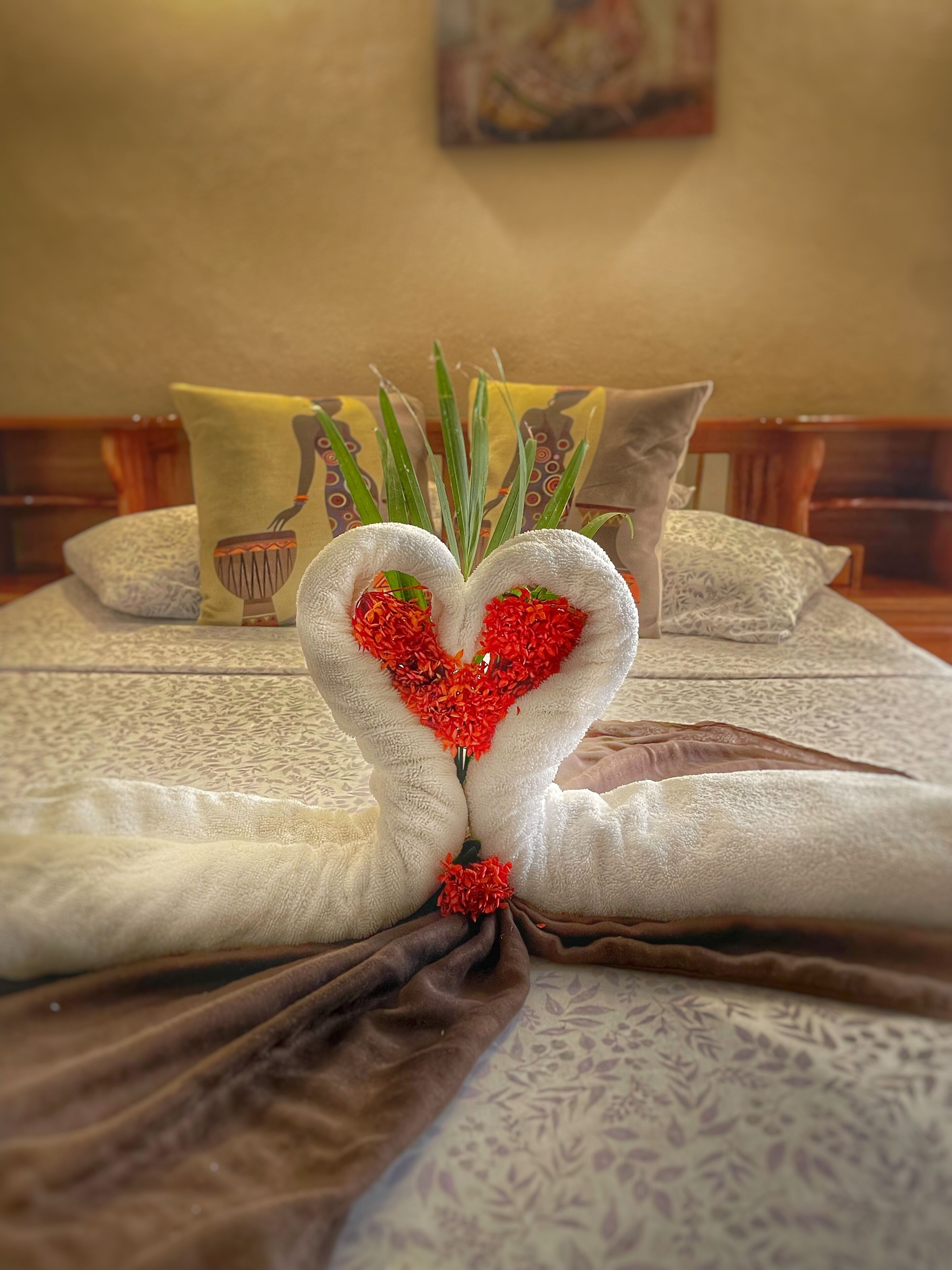 A neatly made bed with a heart-shaped towel arrangement and decorative pillows.