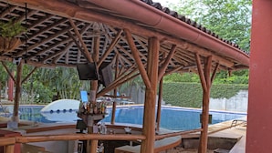 A covered outdoor bar area with a pool in the background. - Hotel Nany (Cabo Velas)