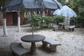 An outdoor seating area with stone tables and benches, surrounded by gravel and plants. - Hotel Nany (Cabo Velas)