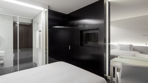 Une chambre d’hôtel moderne avec un lit, un bureau dont le plateau est en verre et un grand miroir.
