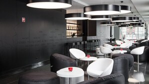 Un espace lounge moderne avec des sièges noirs et blancs, un bar avec des bouteilles et un mur orné de noms de villes.