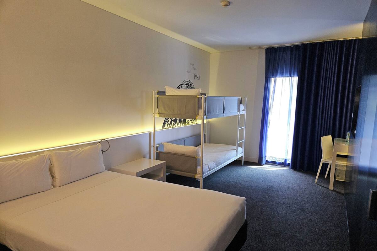 Et hotelværelse med køjeseng, enkelt seng, skrivebord og stol.