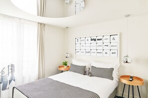 Un dormitorio moderno con una cama grande, un reloj de pared, una mesita de noche con una planta y un adorno en la pared.