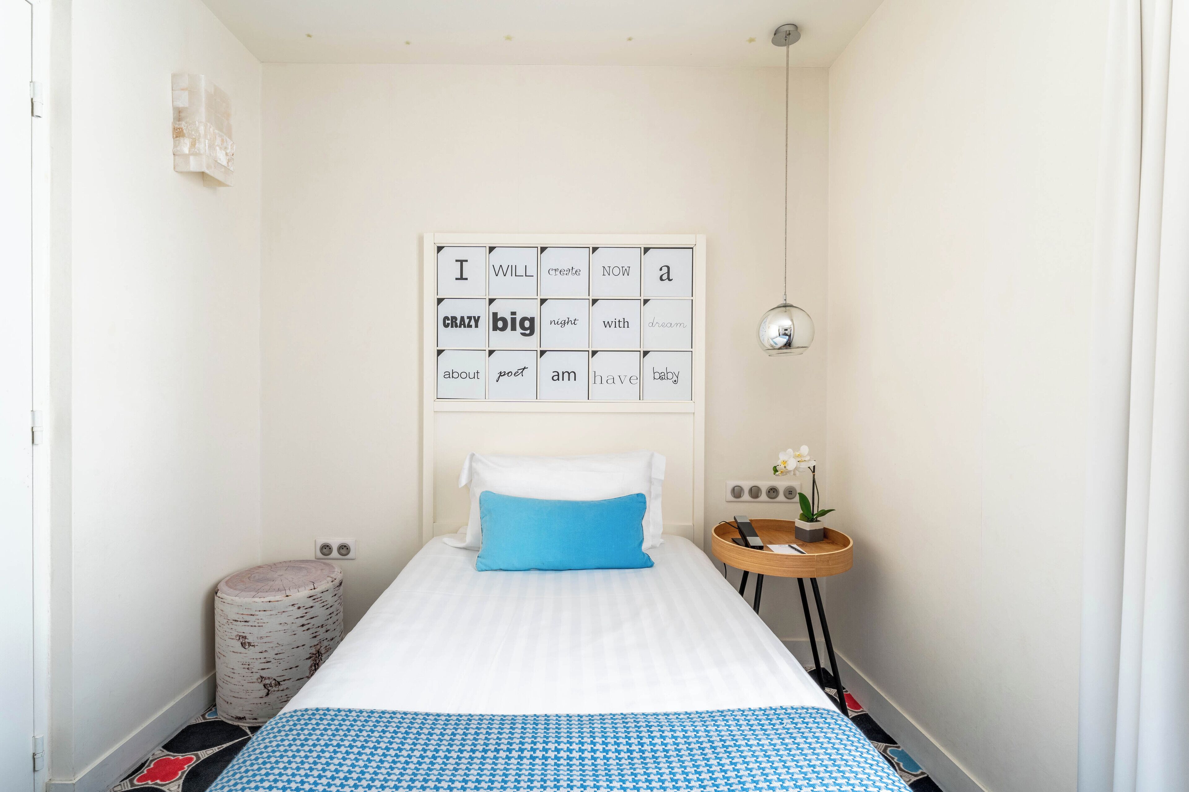 A neatly arranged bedroom with a bed, a small bedside table with a lamp, and a wall-mounted artwork.