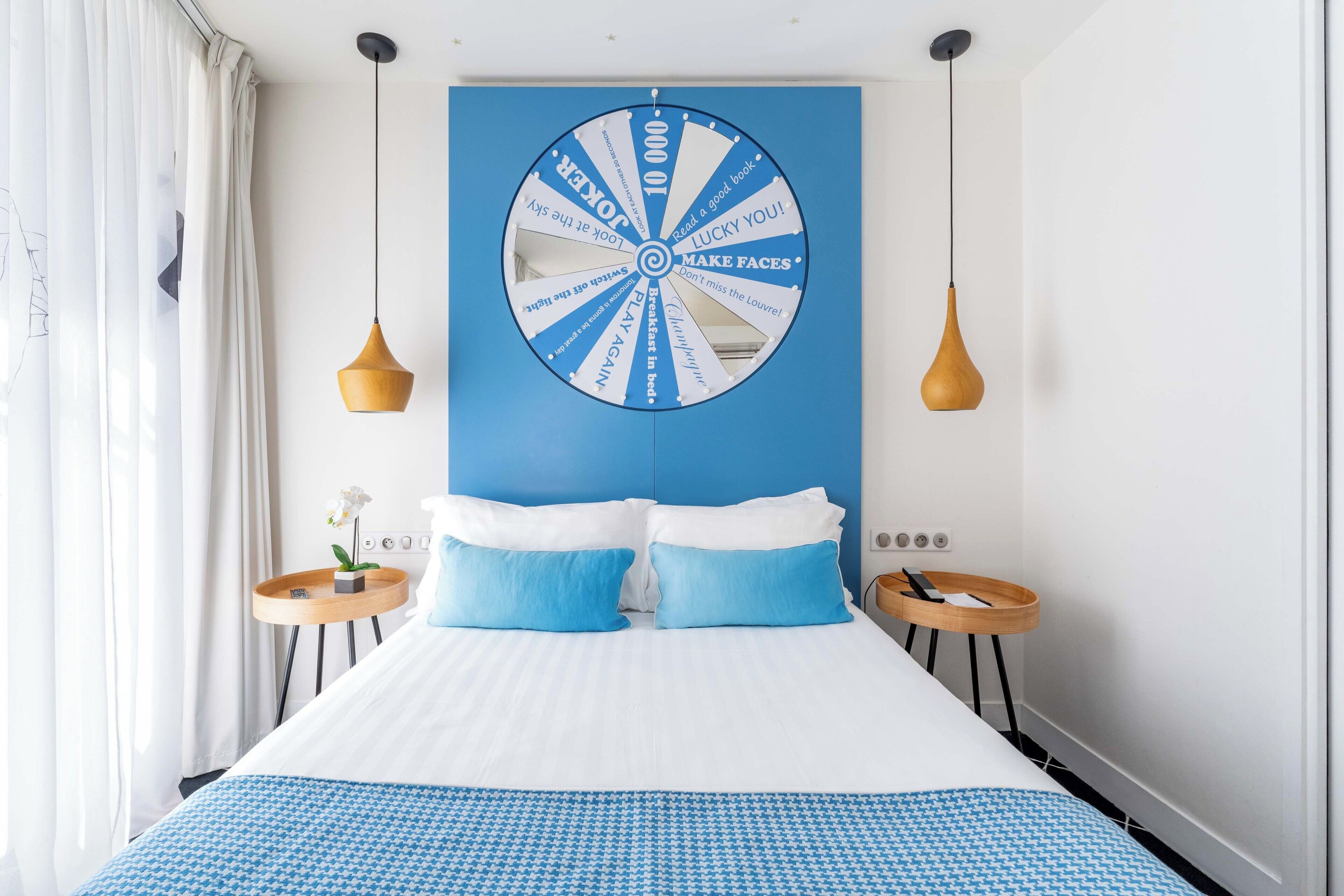 A hotel room with a large bed, two bedside tables, a wall-mounted circular decoration, and pendant lights.