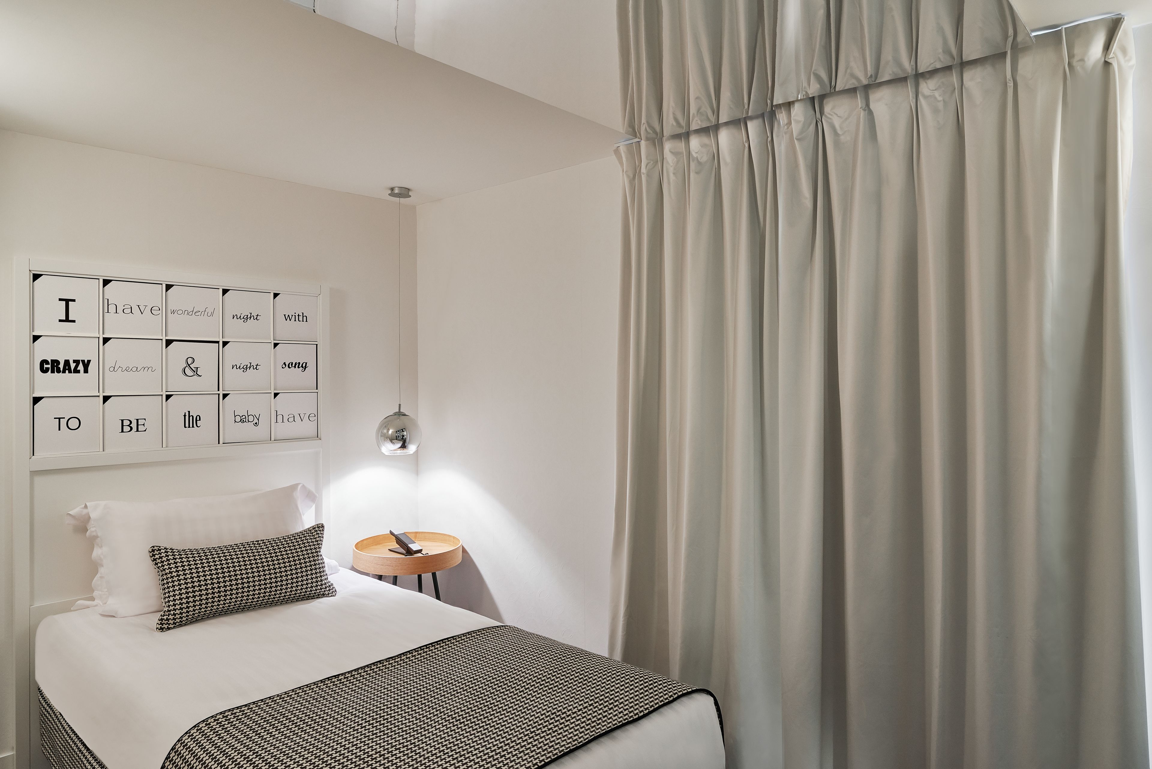 Una camera da letto ordinata con un letto, un comodino con una lampada e una parete decorata con citazioni motivazionali.