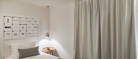 A neatly arranged bedroom with a bed, a bedside table with a lamp, and a wall with motivational quotes.